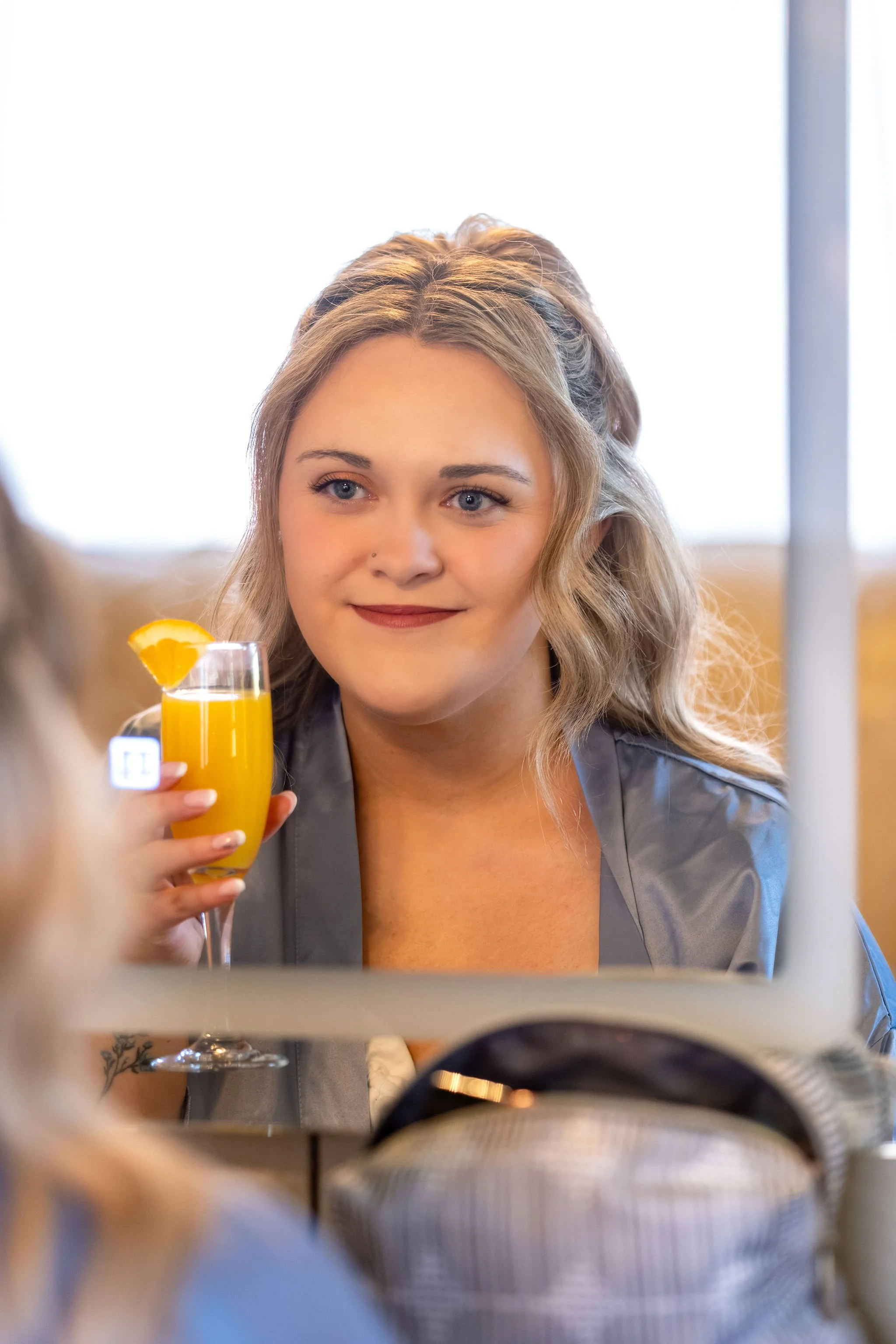 Ellie smiling at her reflection while holding a mimosa in a gray satin robe at Boothbay Playhouse in Boothbay Maine fall wedding photography VMG Productions