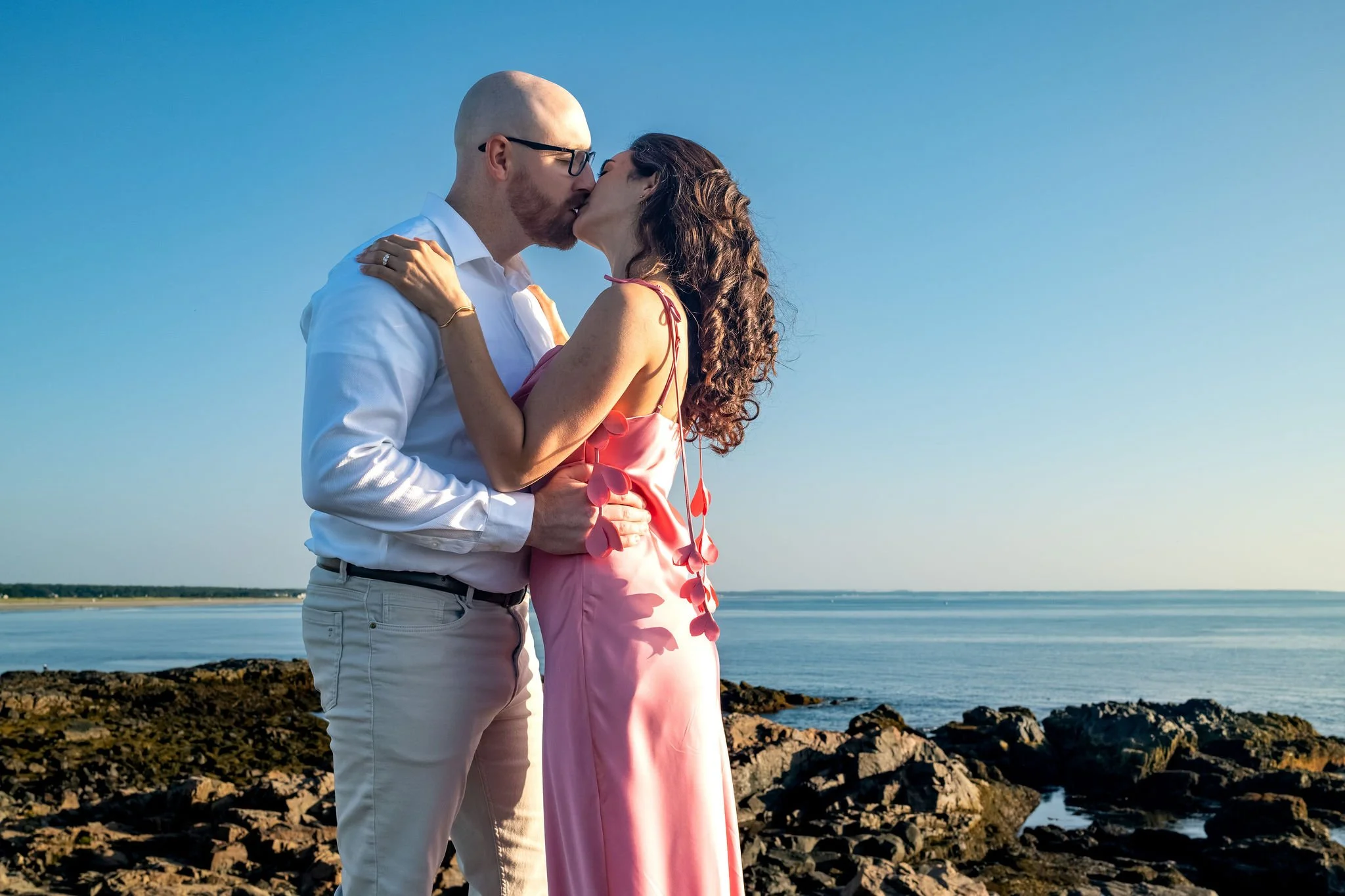 Zack and Helena kissing on the rocks with the calm ocean and horizon behind them on Marginal Way in Ogunquit Maine sunrise proposal and engagement photography VMG Productions