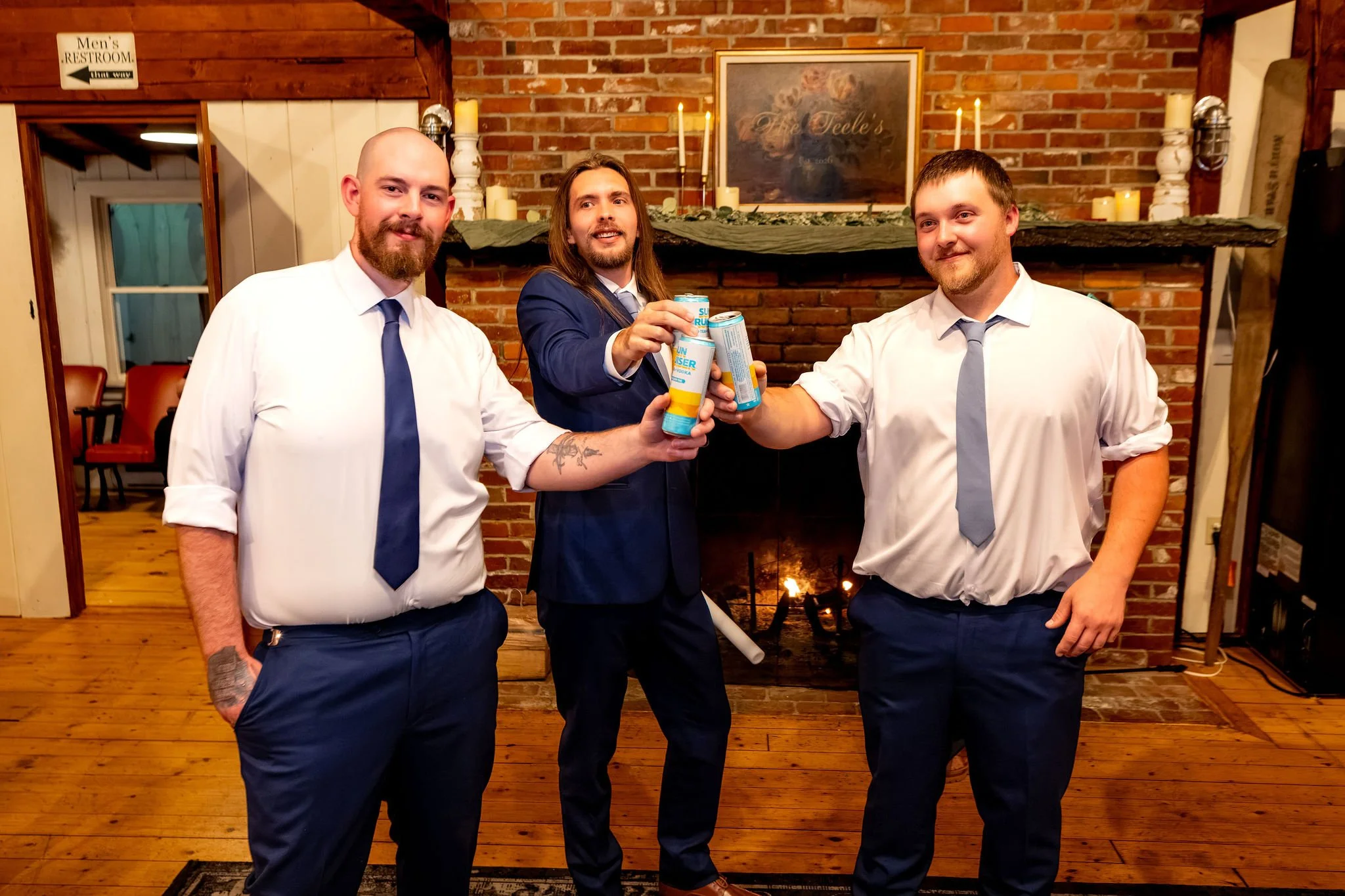 Sam and two groomsmen toasting with canned drinks in front of the brick fireplace at Boothbay Playhouse in Boothbay Maine fall wedding photography VMG Productions