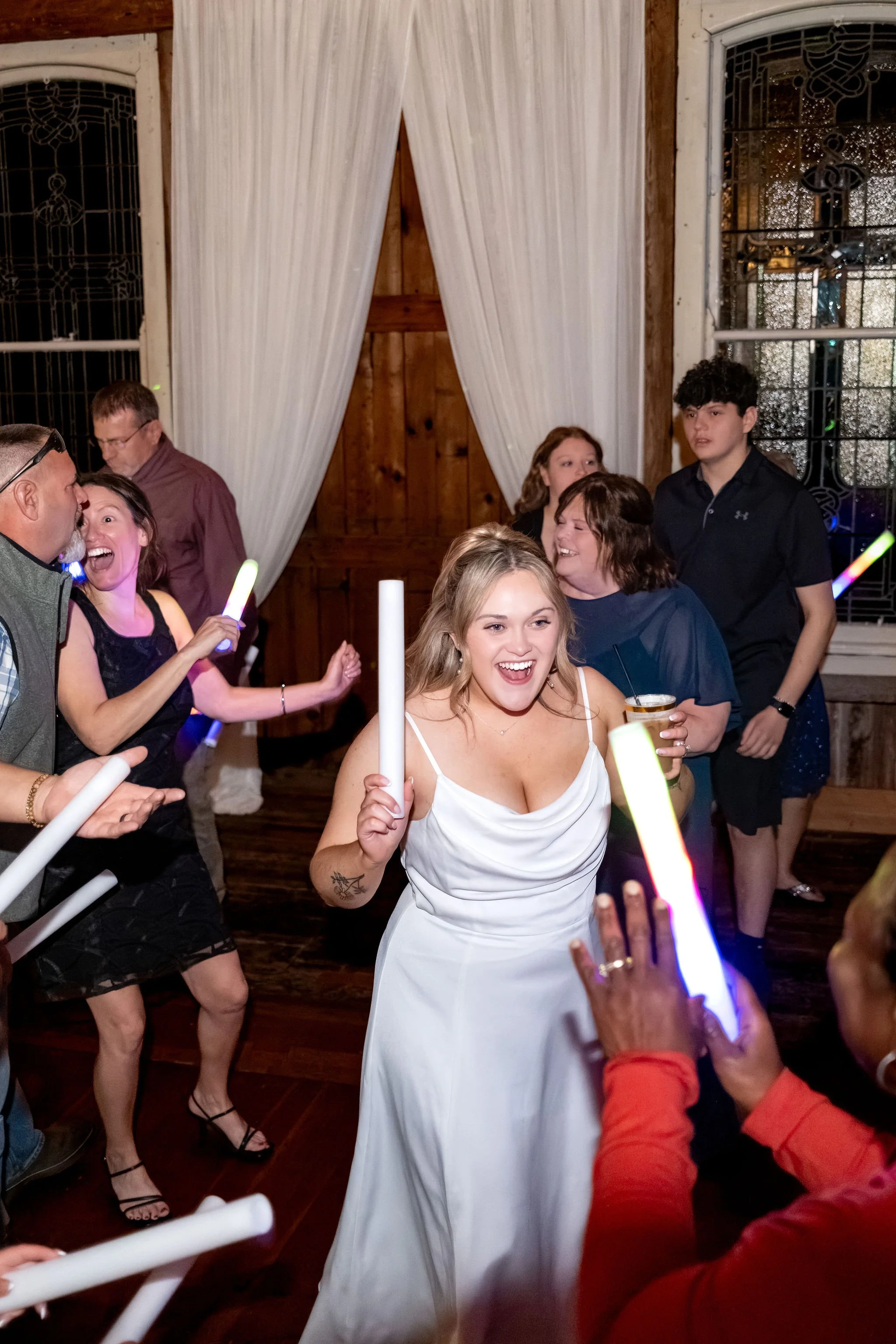 Ellie smiling wide with a glow stick in her hand as friends dance around her at Boothbay Playhouse in Boothbay Maine fall wedding photography VMG Productions