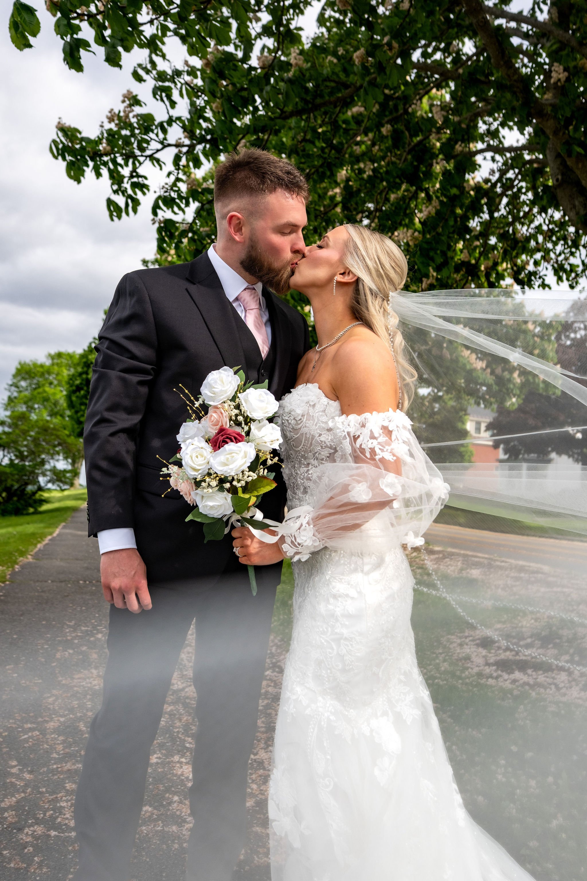 Jeremiah and Vienna classic portrait of the couple sharing a kiss beneath the tree canopy at Eastern Promenade Portland Maine spring wedding photography VMG Productions