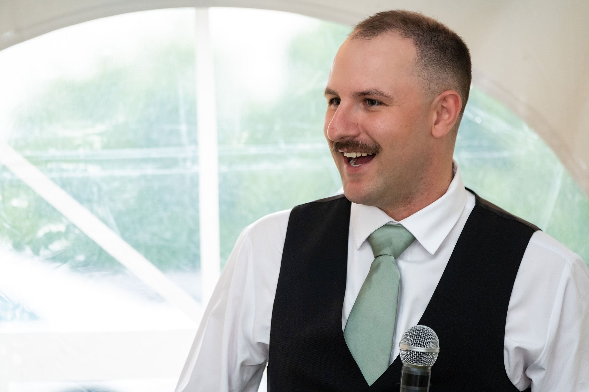 Ethan DeAngelis best man laughing mid-speech inside the reception tent at the Sanbornton New Hampshire wedding photography VMG Productions
