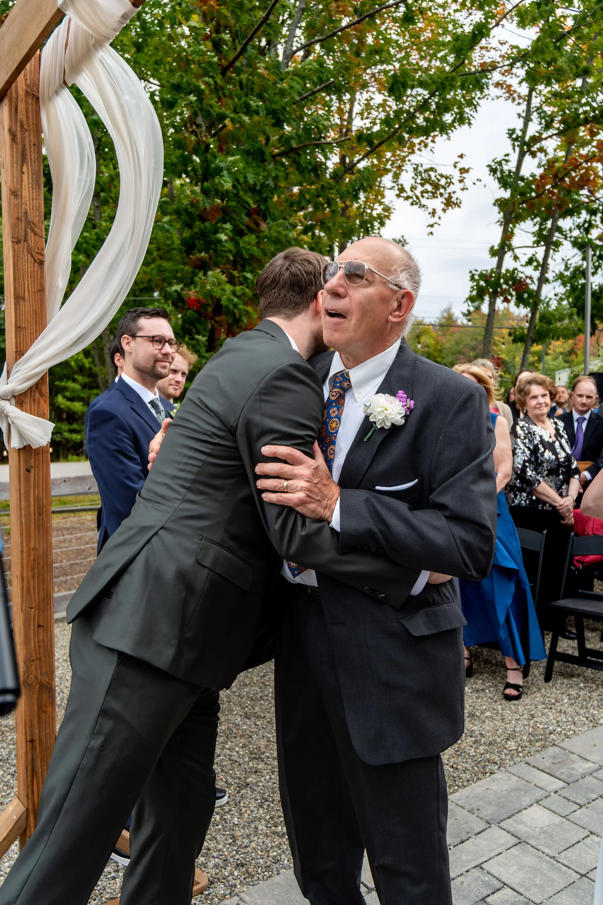 Jack hugging Victoria's dad at the front of the aisle at The Cellars at Allagash Brewing Company in Portland Maine fall wedding photography VMG Productions