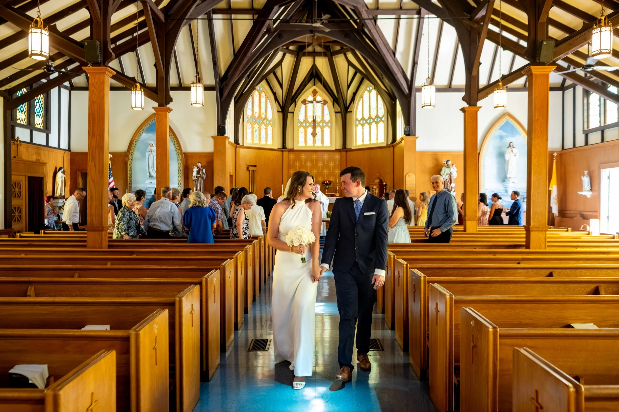 Caroline and Anthony Pirolli walking back up the aisle as a married couple beneath the timber-frame ceiling at Star of the Sea in York Maine wedding photography VMG Productions