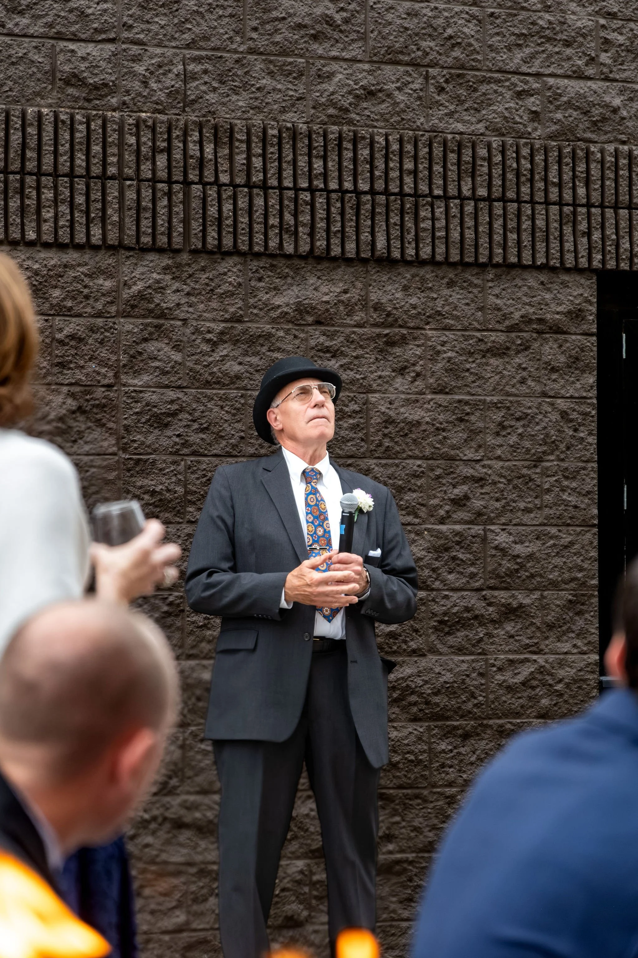 Victoria's dad in a bowler hat looking up as he gives his toast on the patio at The Cellars at Allagash Brewing Company in Portland Maine fall wedding photography VMG Productions