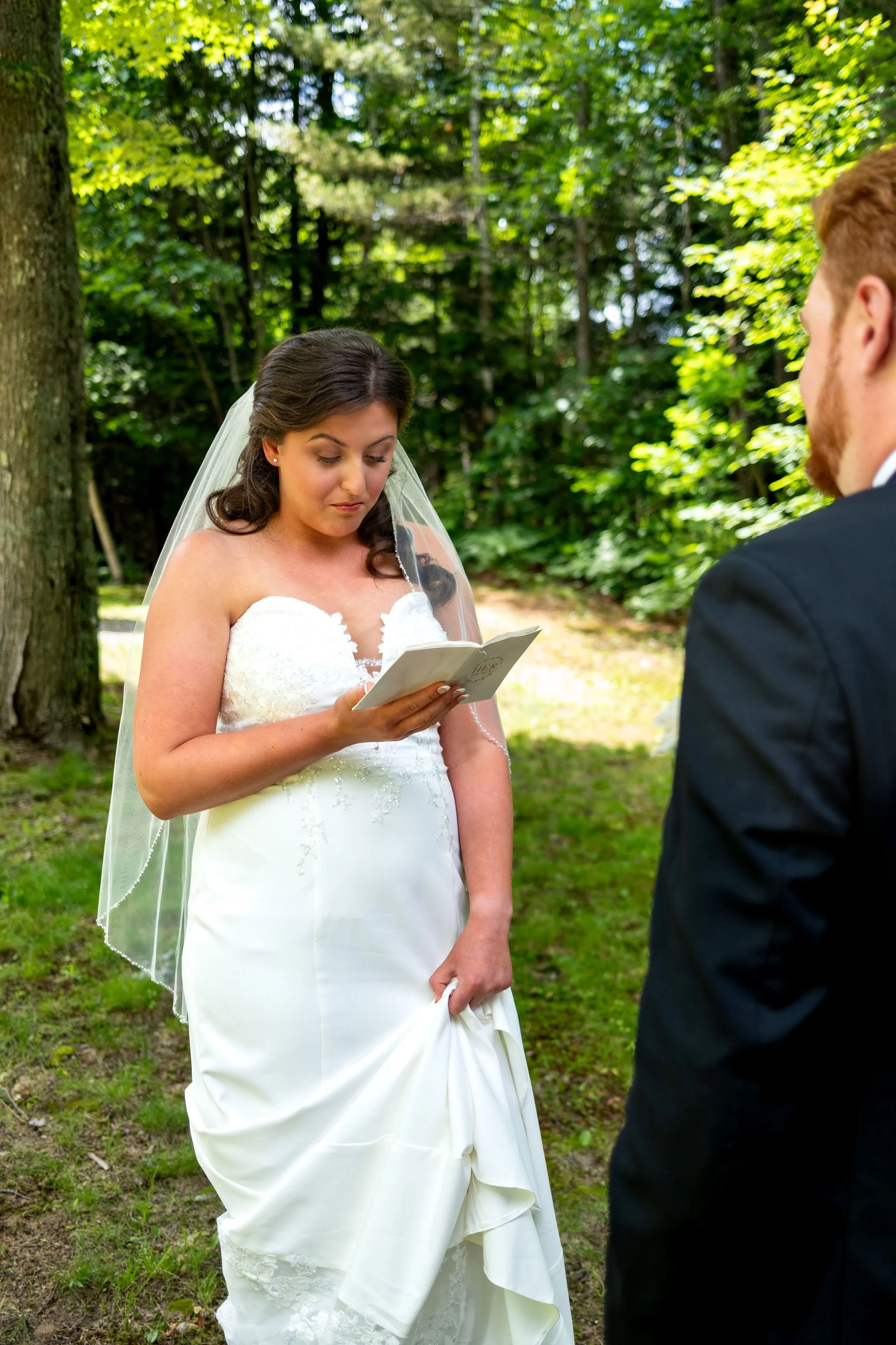 Alyssa and Colby the bride reading her private vows from a small white book during the first look in Bethel Maine summer wedding photography VMG Productions