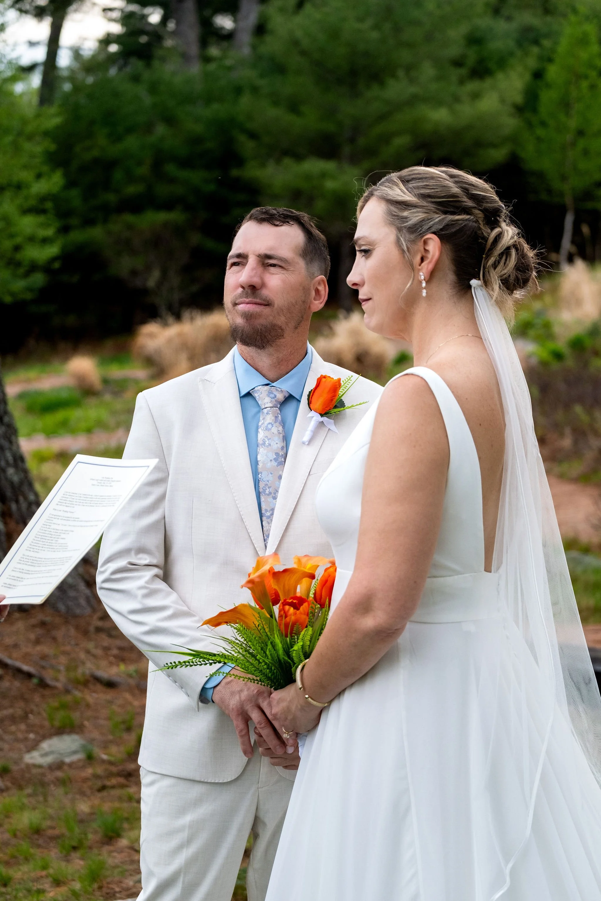 Alli and Adam Baudoin holding hands during their ceremony vows under the pines in Mount Desert Maine spring wedding photography VMG Productions