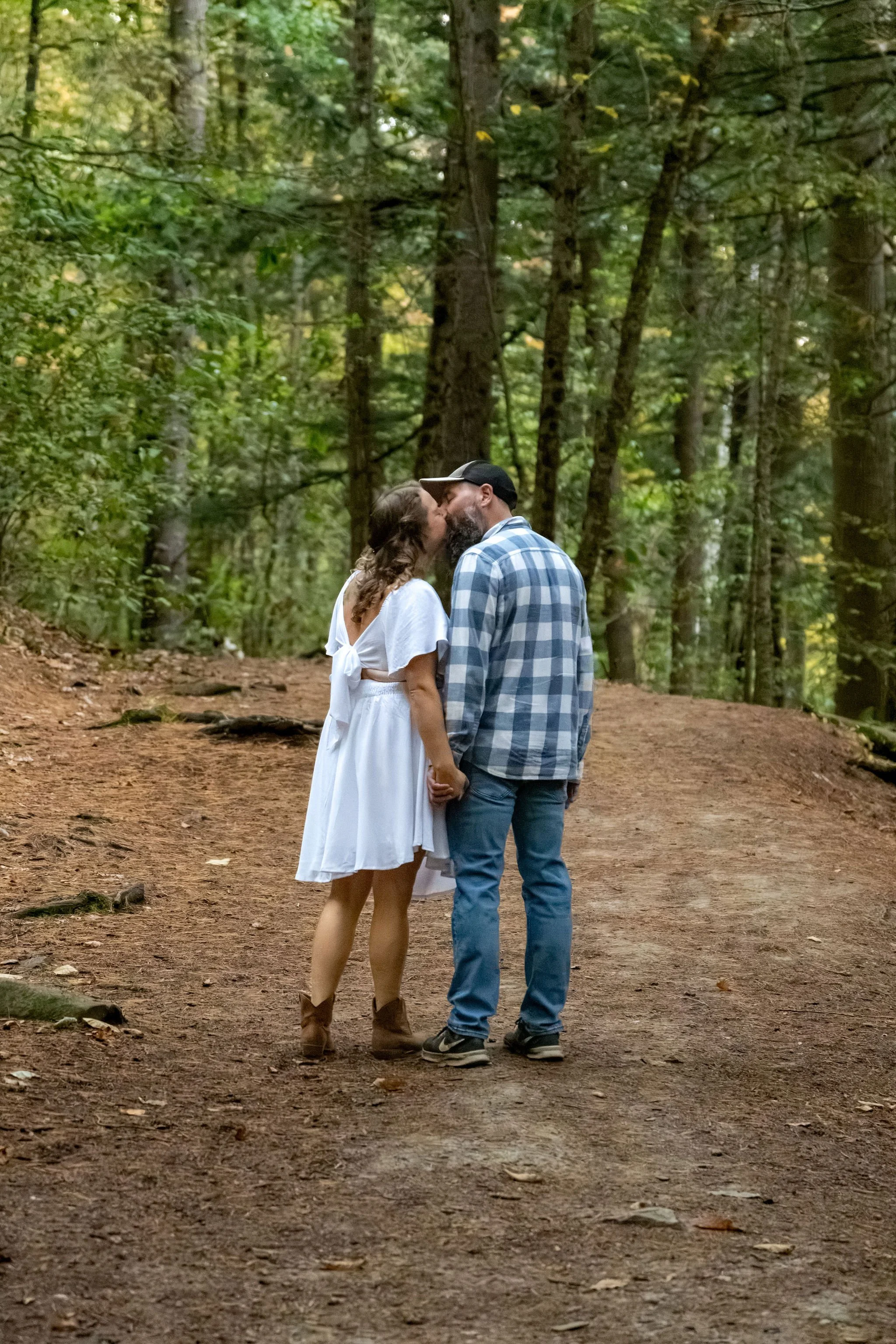 Alison and Dave kissing on the trail with the tall trees around them at Vaughan Woods in Hallowell Maine fall engagement photography VMG Productions