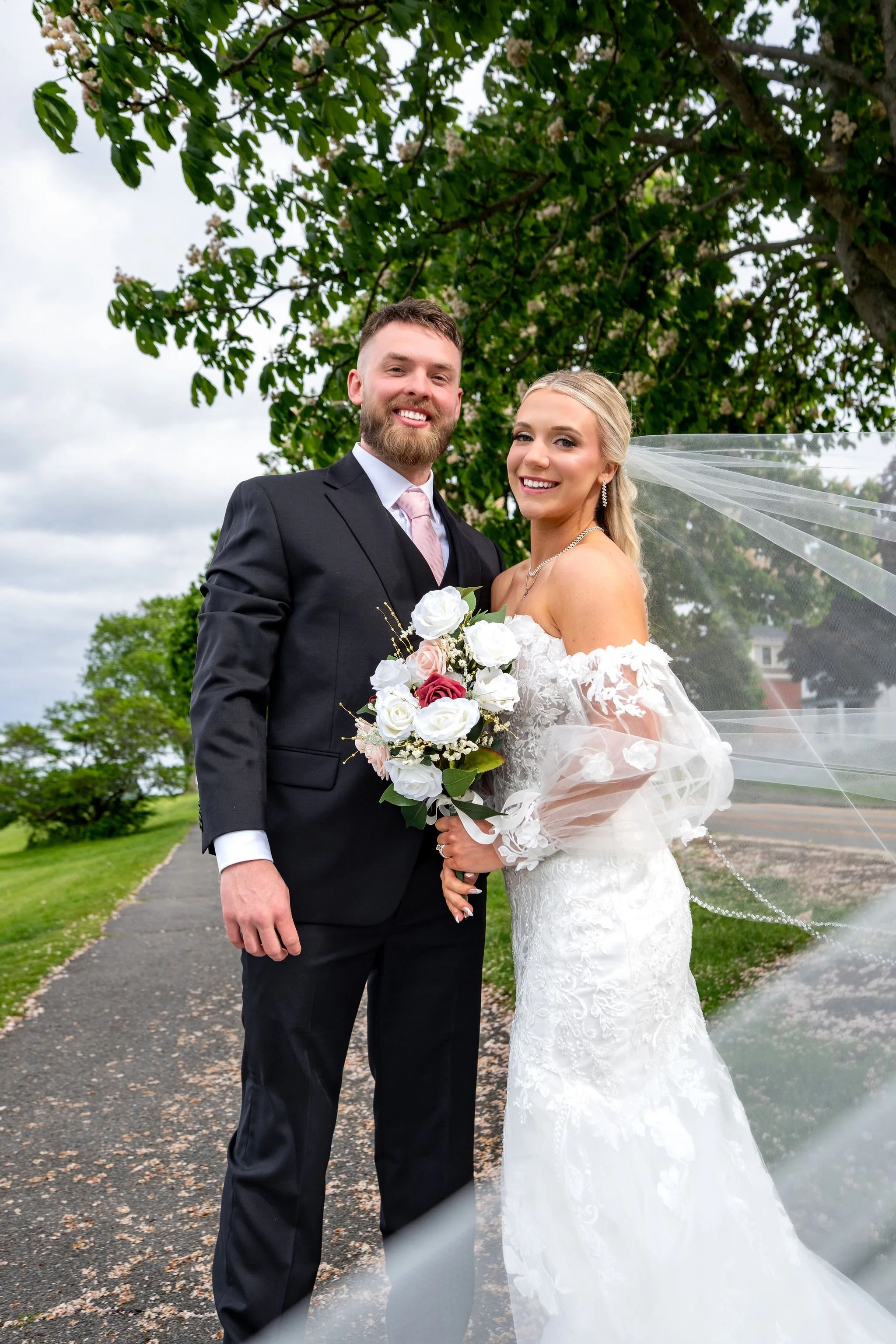 Jeremiah and Vienna full-length portrait of the couple standing together beneath flowering branches at Eastern Promenade Portland Maine spring wedding photography VMG Productions