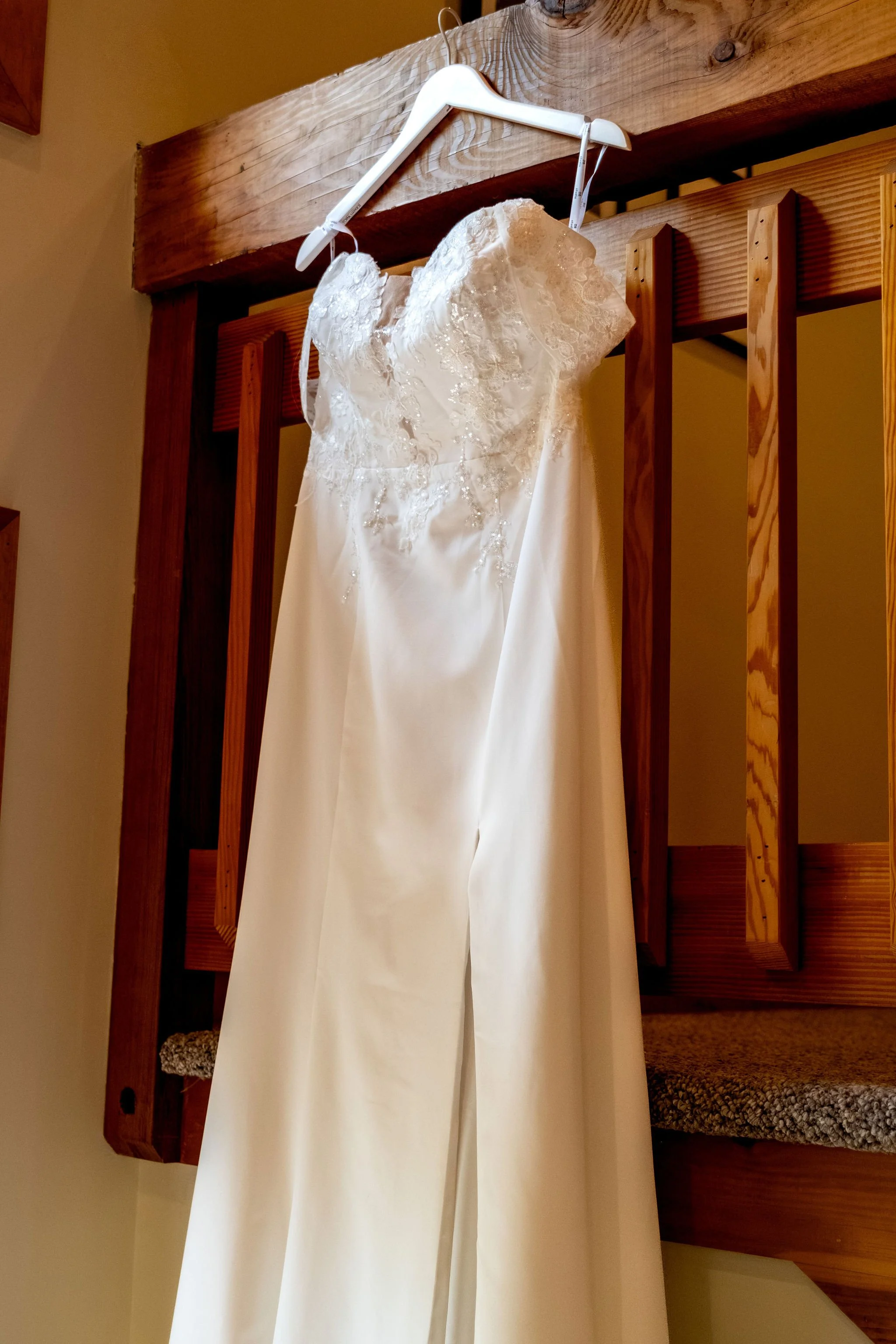 Alyssa and Colby lace wedding dress hanging from a wooden beam during morning preparations in Bethel Maine summer wedding photography VMG Productions