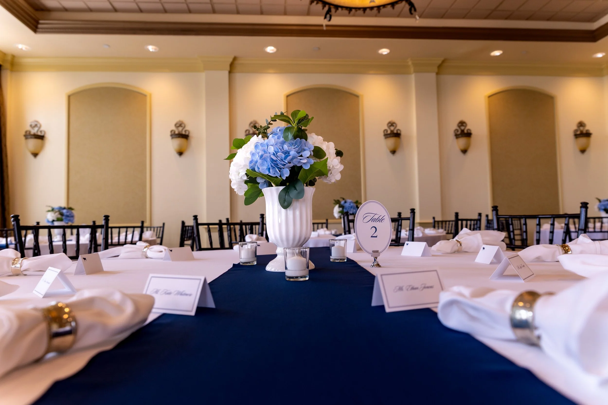 Blue and white hydrangea centerpiece with calligraphy place cards and candles along the navy table runner at Union Bluff Hotel in York Maine wedding photography VMG Productions