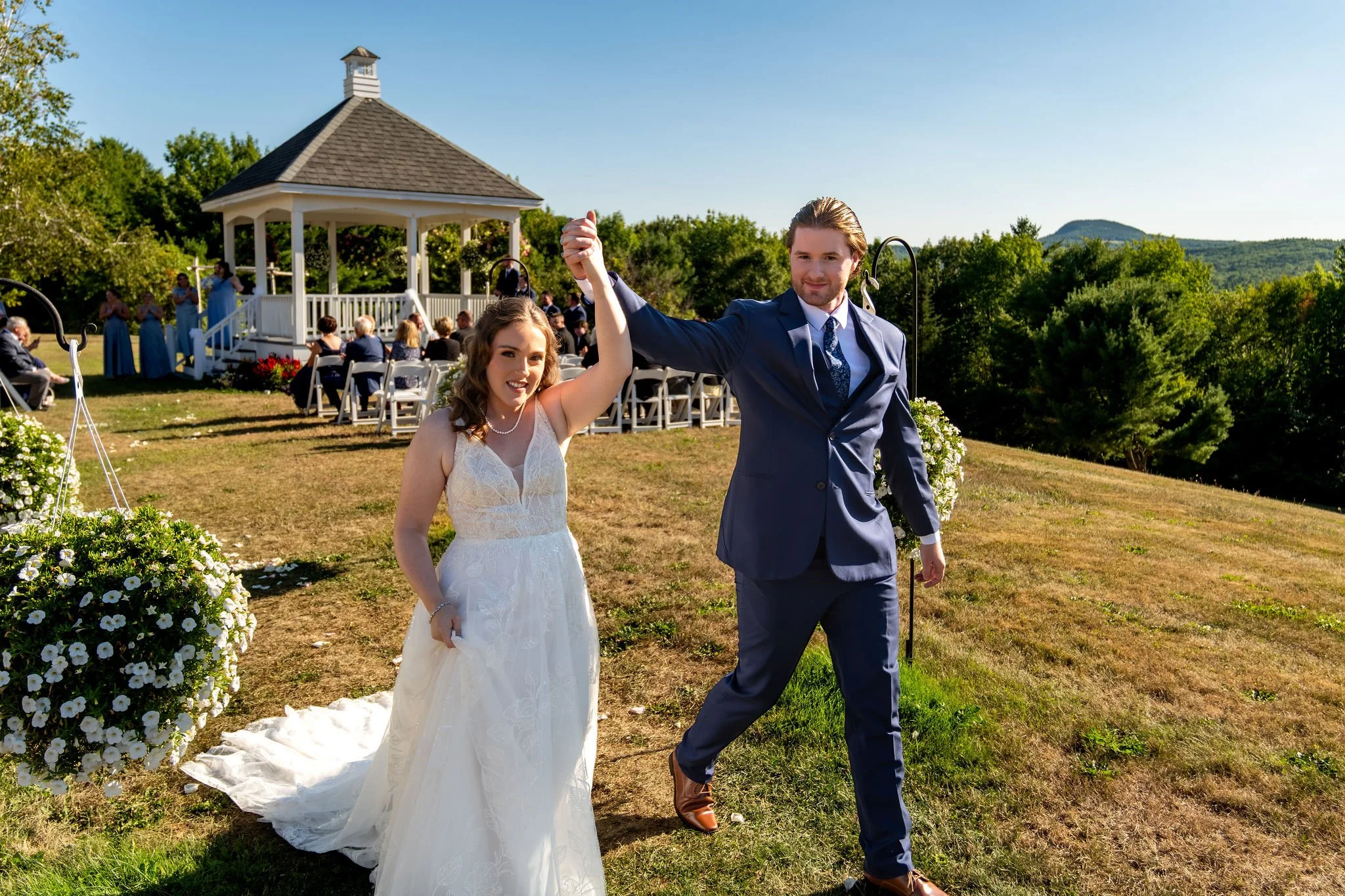 Zachary and Hollie raising their arms as they walk back down the aisle from the hilltop gazebo at The Lucerne Inn in Dedham Maine summer wedding photography VMG Productions