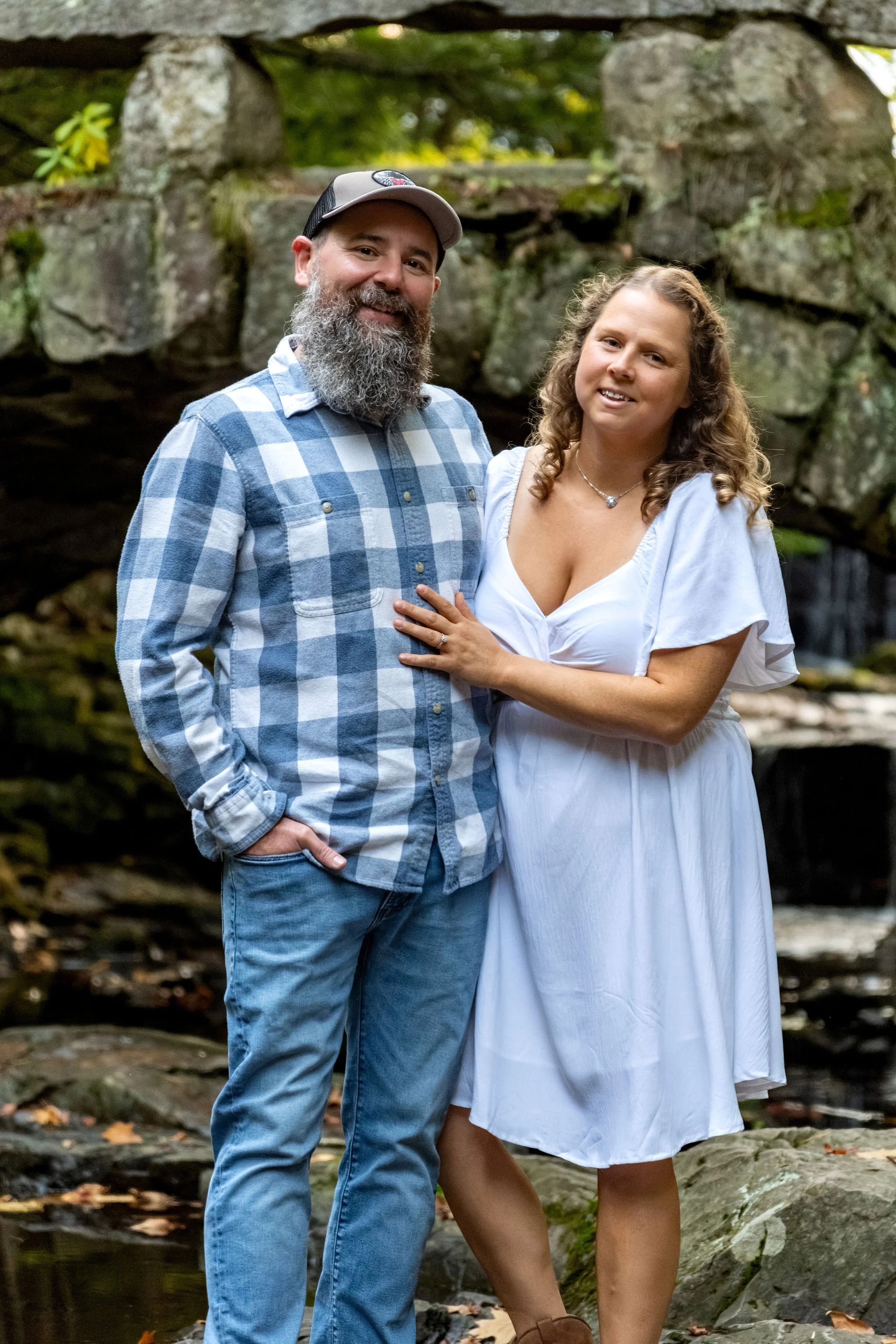 Dave with his arm around Alison as they smile under the stone arch bridge at Vaughan Woods in Hallowell Maine fall engagement photography VMG Productions
