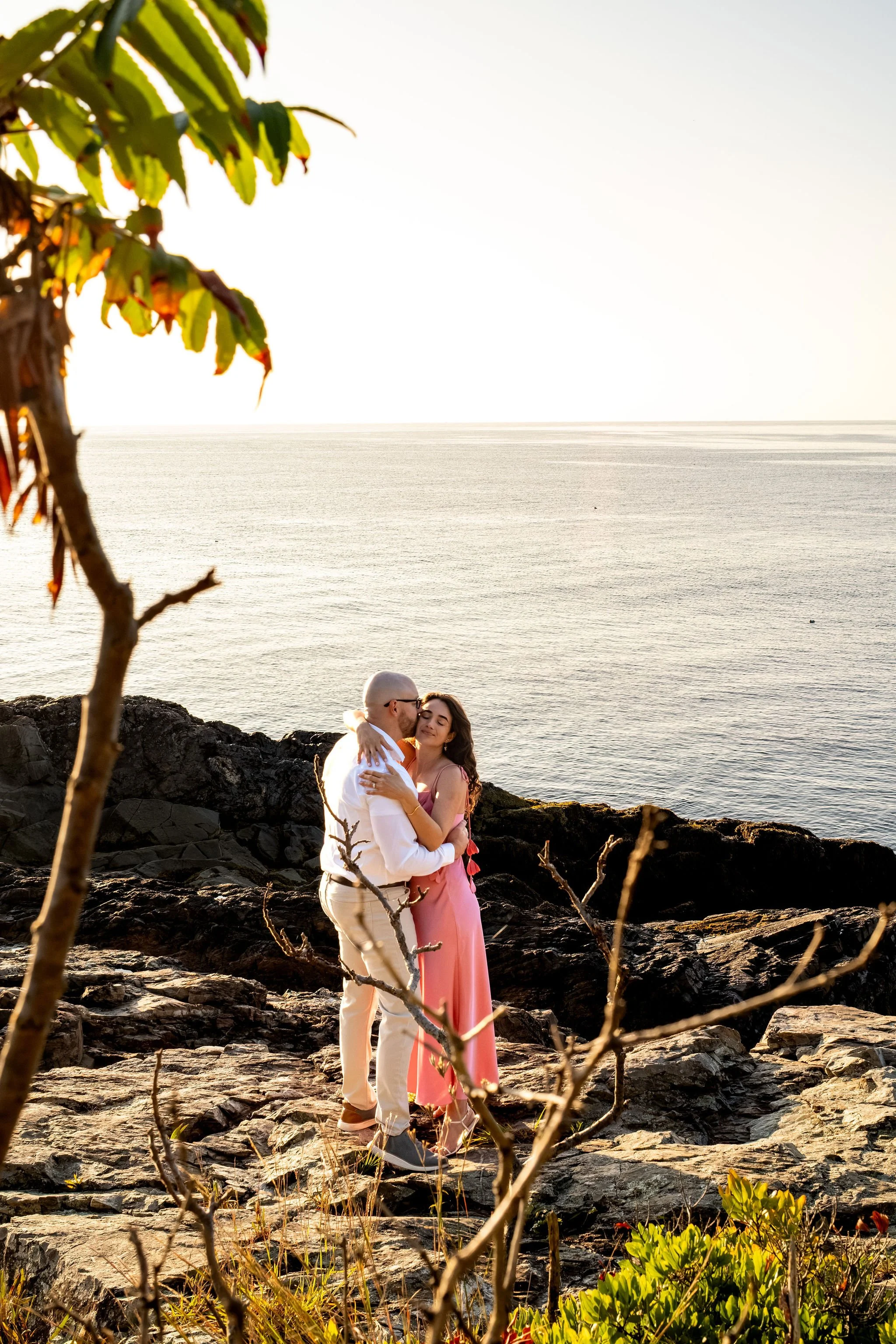Zack and Helena kissing on a rocky ledge with the ocean stretching out behind them on Marginal Way in Ogunquit Maine sunrise proposal and engagement photography VMG Productions