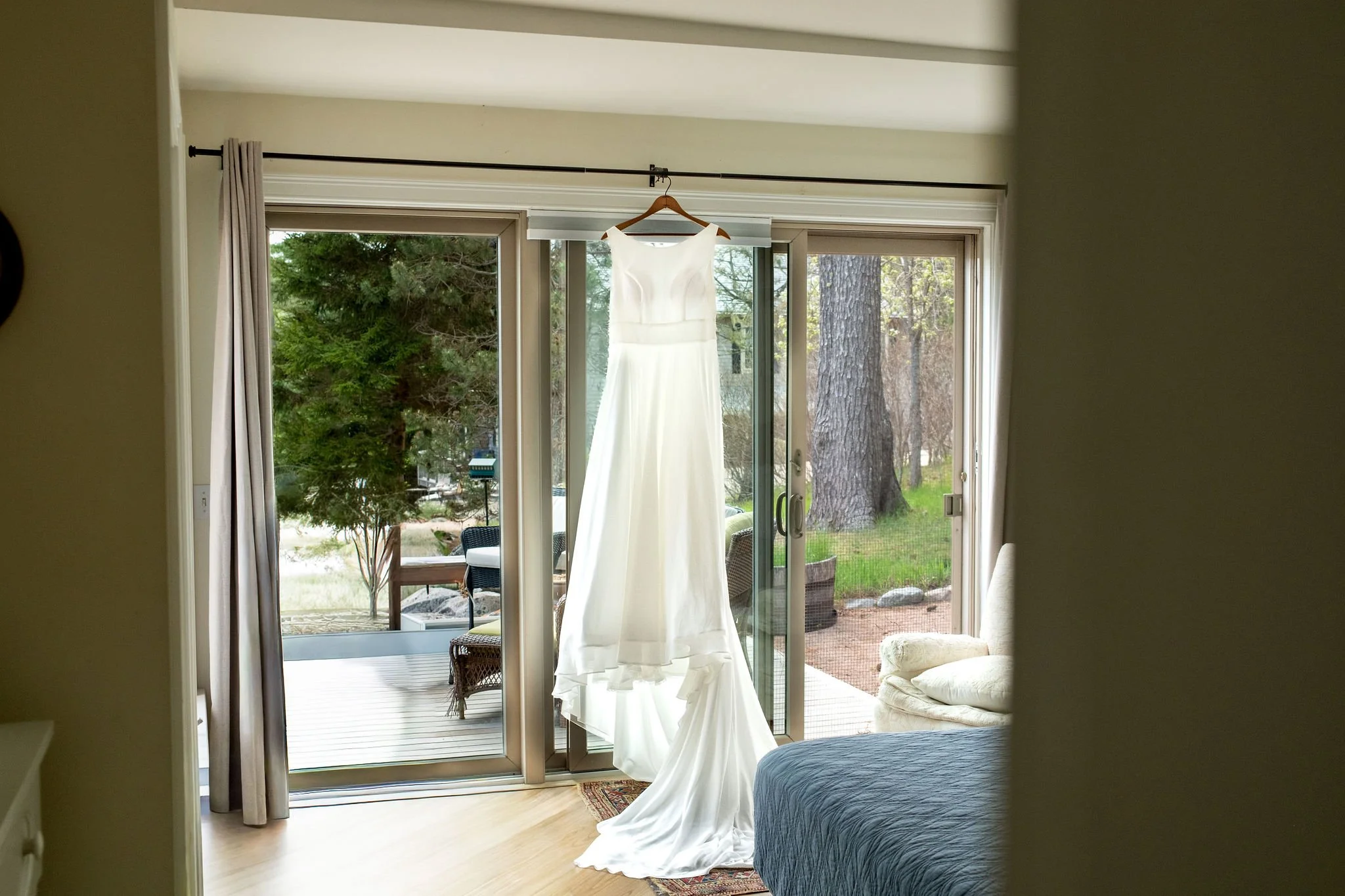 Alli Baudoin's wedding dress hanging in the window light at a private residence overlooking Somes Sound in Mount Desert Maine spring wedding photography VMG Productions