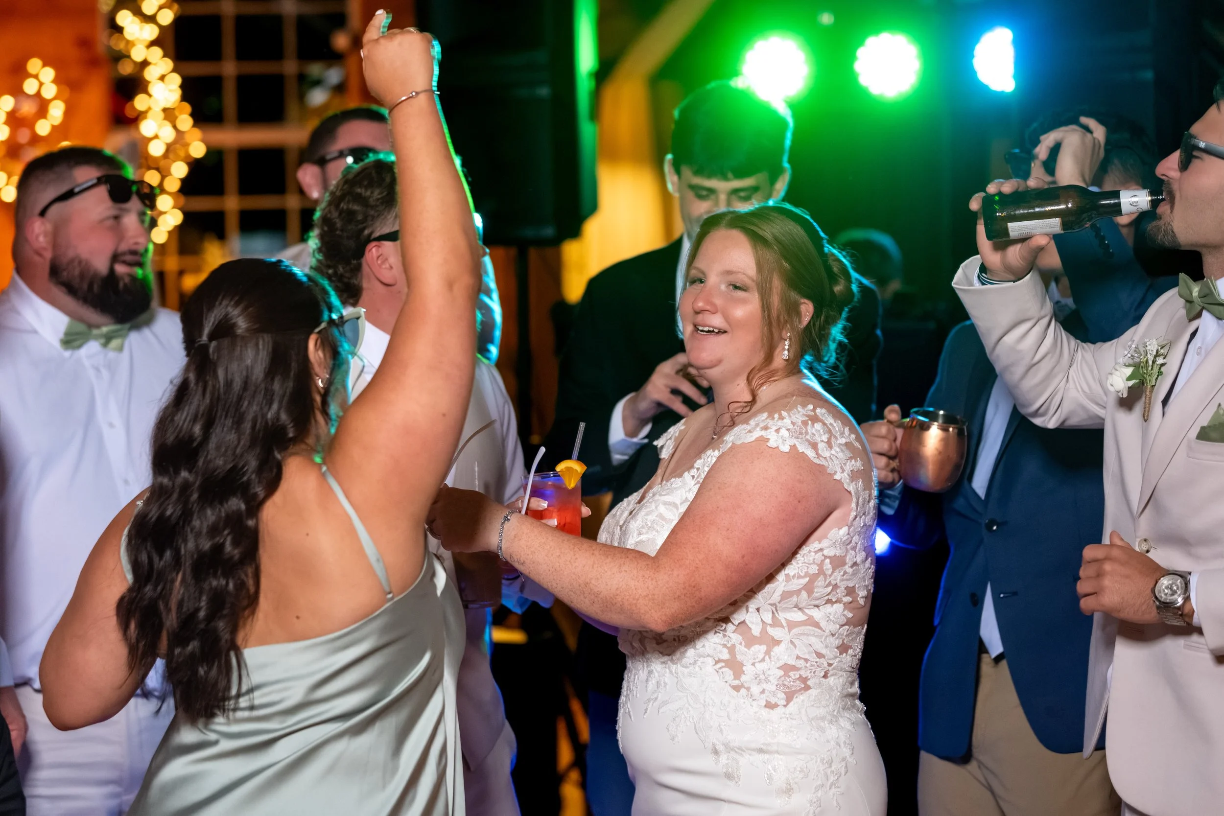 Erika in her wedding dress dancing with a bridesmaid under green and blue lights at the Maine Wedding Barn and Event Center in Minot Maine fall wedding photography VMG Productions