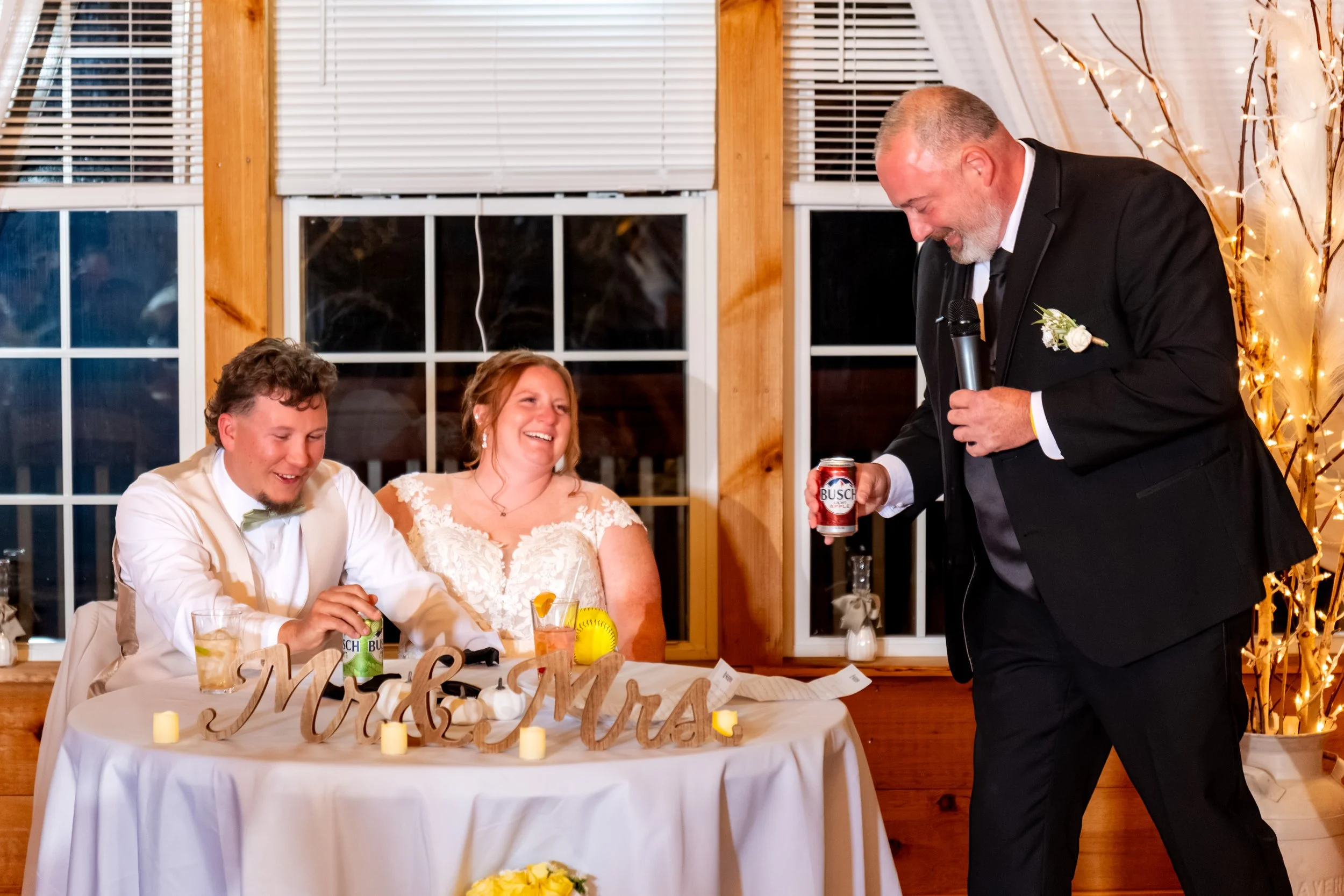 Erika's dad standing with a glass raised at the head table as Erika and Andrew listen at the Maine Wedding Barn and Event Center in Minot Maine fall wedding photography VMG Productions