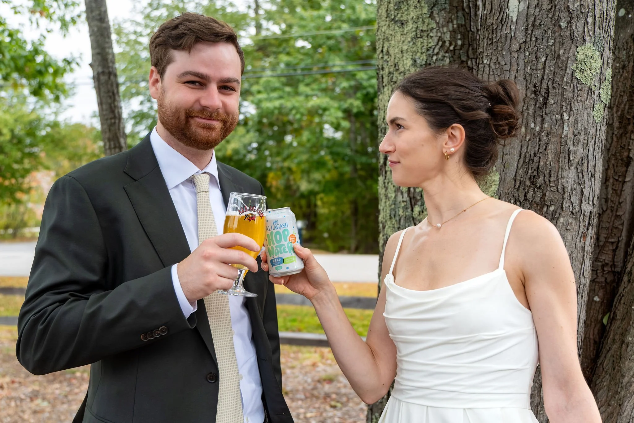 Jack and Victoria clinking a glass of beer and an Allagash can before the ceremony at The Cellars at Allagash Brewing Company in Portland Maine fall wedding photography VMG Productions