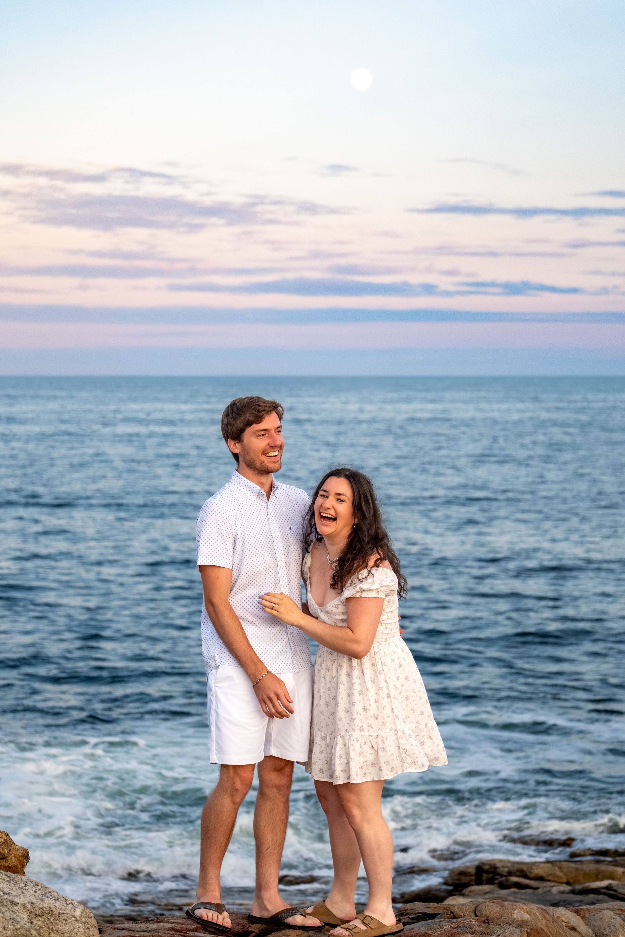 Kirstie laughing with Lucas as the moon rises over the ocean behind them at Reid State Park in Georgetown Maine engagement photography VMG Productions