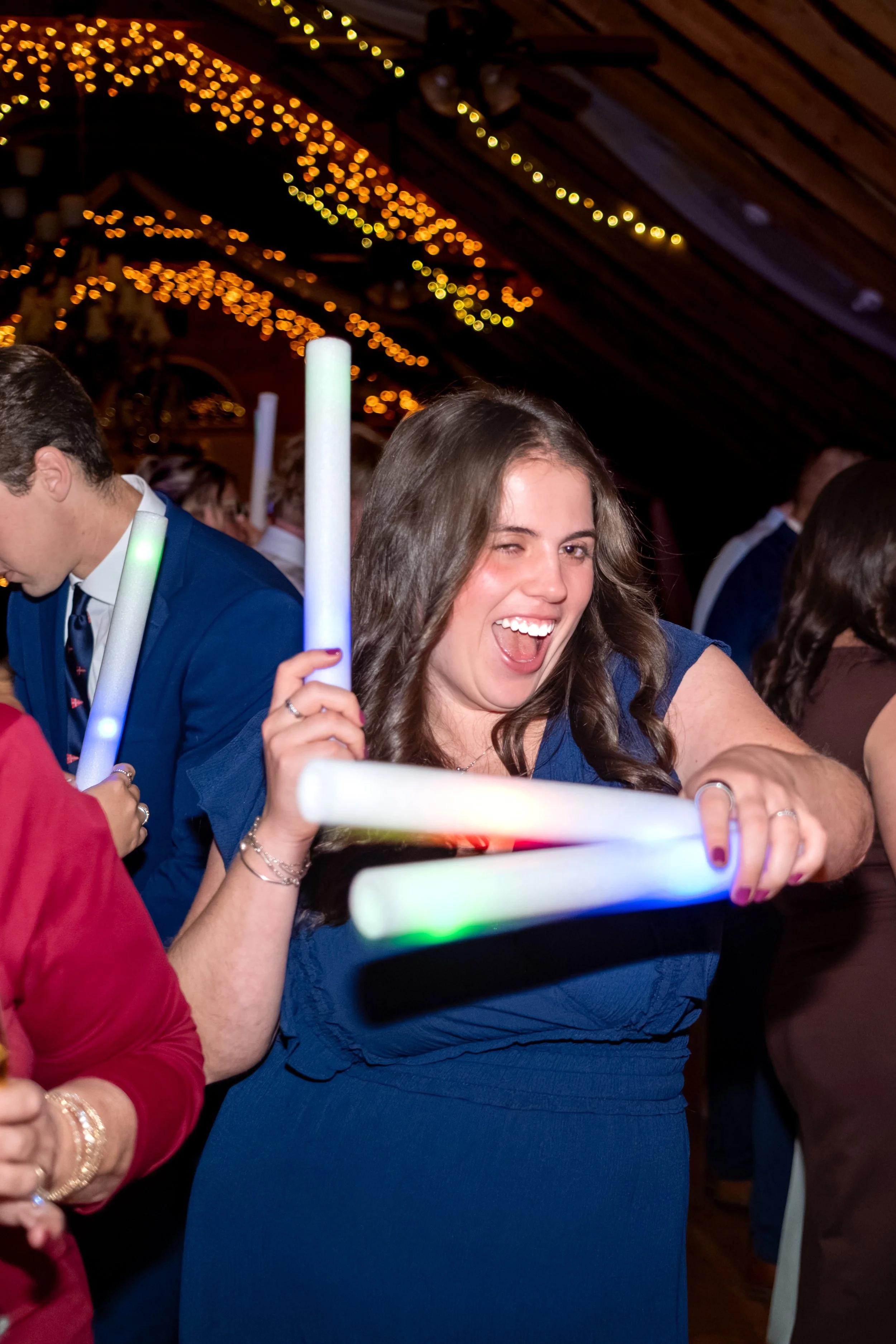 A guest in a navy dress laughing with a pair of light-up wands in her hands at the Maine Wedding Barn and Event Center in Minot Maine fall wedding photography VMG Productions