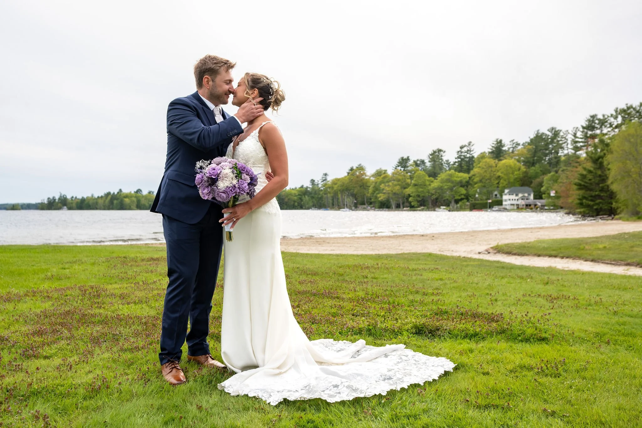 Beth and Cameron sharing a kiss by the lake after the ceremony at Augusta Country Club Manchester Maine spring wedding photography VMG Productions