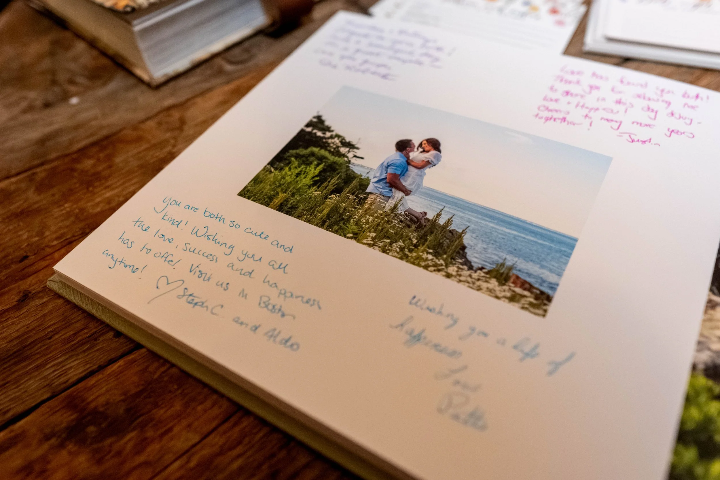 Close up of printed guest book album page at Mountain Star Estate Rangeley Maine wedding showing couple embracing in Maine coastal wildflower field engagement photo surrounded by handwritten guest messages and wishes