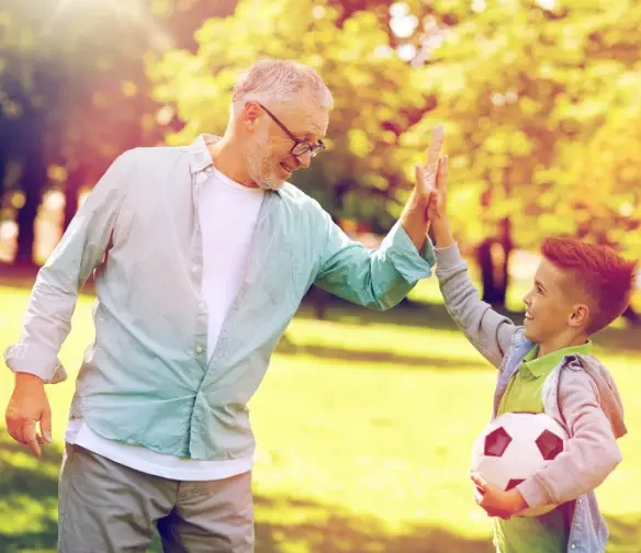 Older man high-fiving child after playing sport, illustrating active lifestyle due to a Bethany pain management doctor.