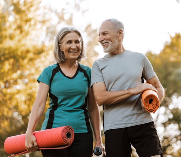 Happy older couple walking outside with yoga mats indicating successful Classen-Ten-Penn pain management doctor care