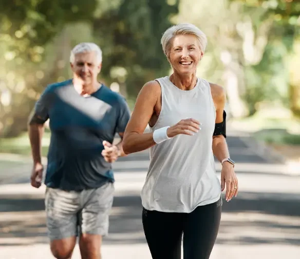 Happy older couple running in park after care from Midwest City pain management doctor.