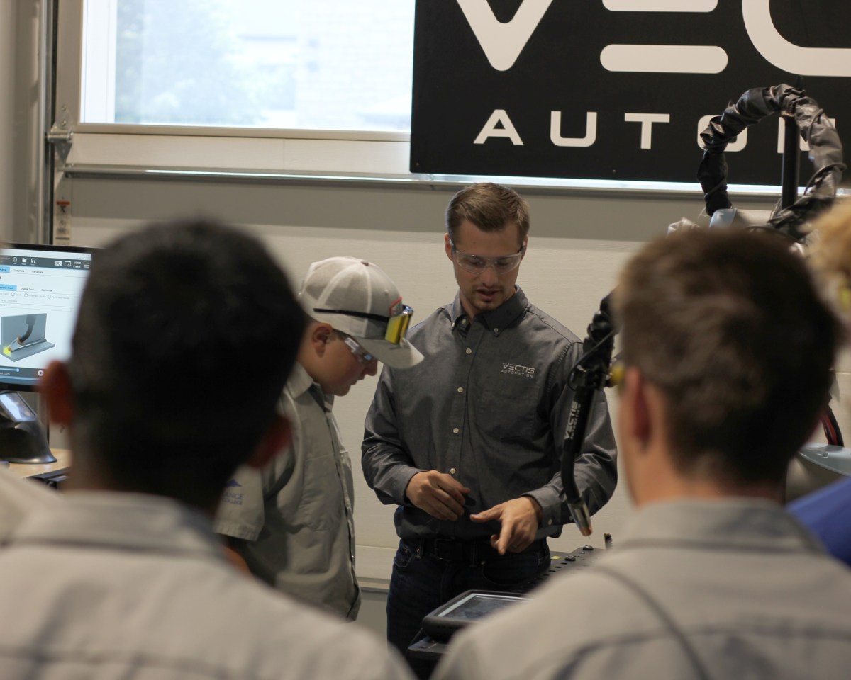 Vectis instructor demonstrating robotic welding technology to students during hands-on manufacturing workforce training.