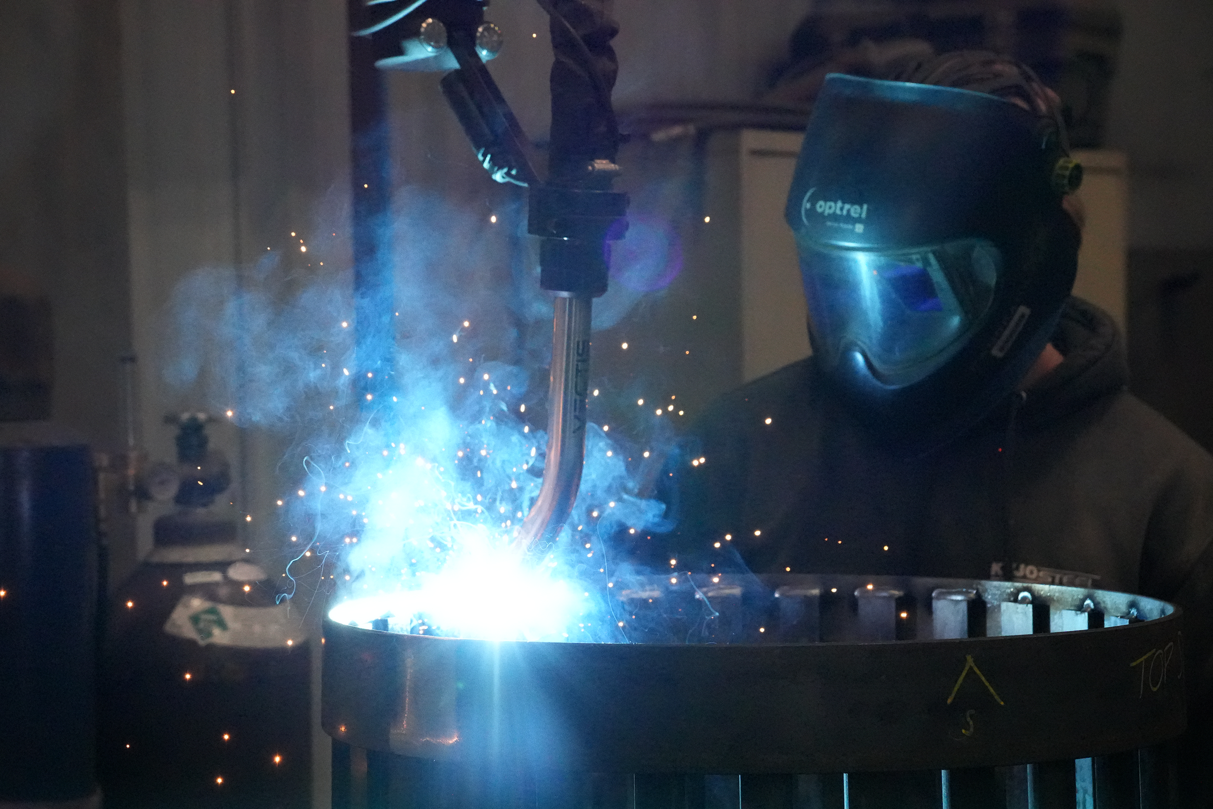 Automated welding robot creating sparks during precision metal fabrication in a contract manufacturing shop.