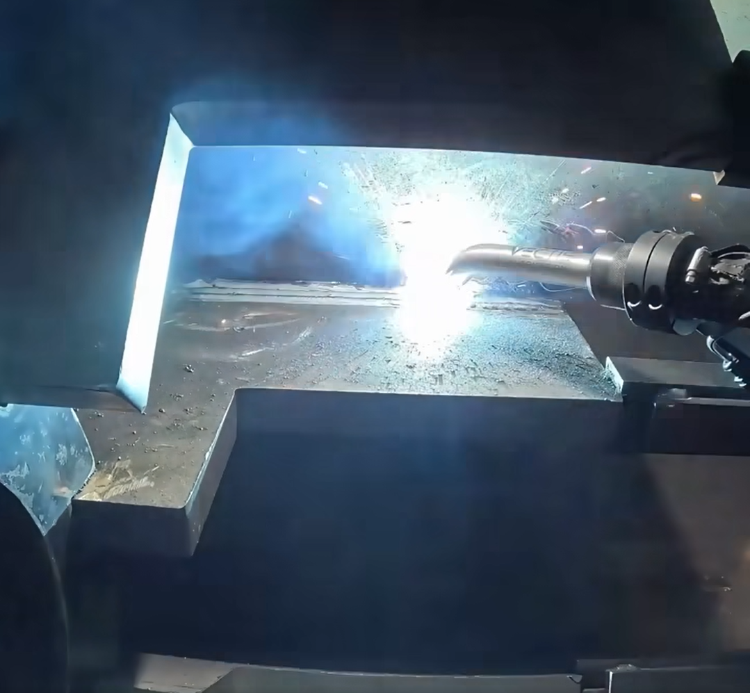 Automated welding torch producing sparks while joining heavy steel plates for shipbuilding in a marine fabrication shipyard.