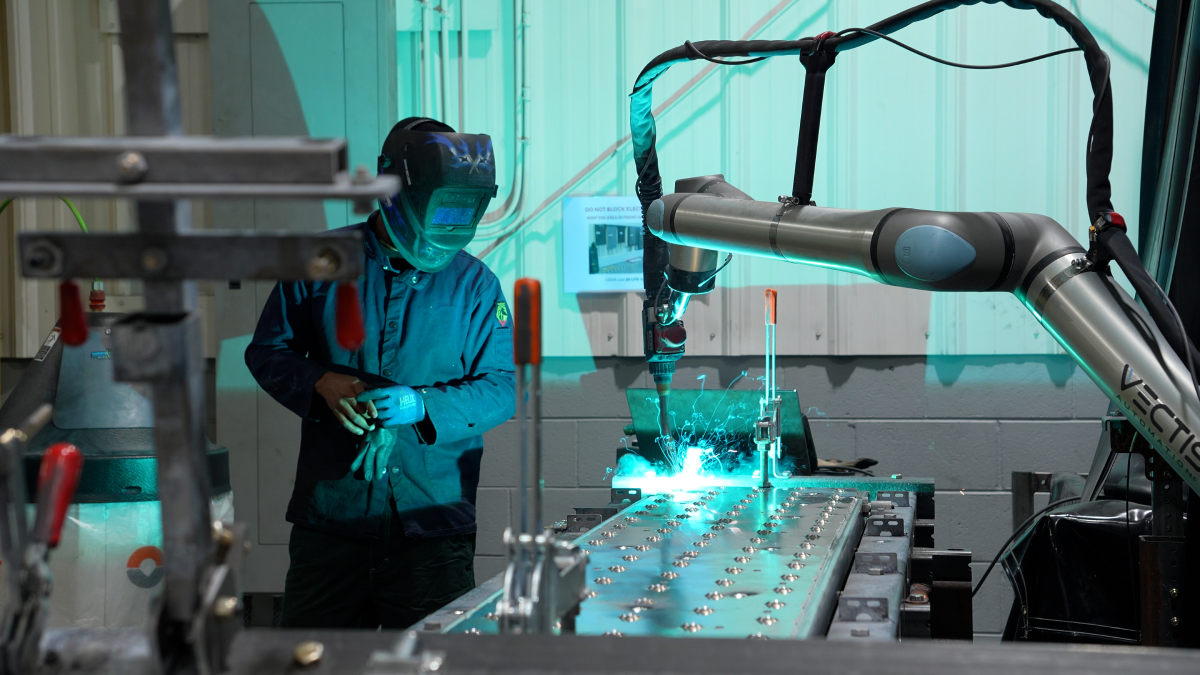 Vectis robotic welding system performing precision aluminum fabrication while an operator monitors the welding process in a manufacturing environment.