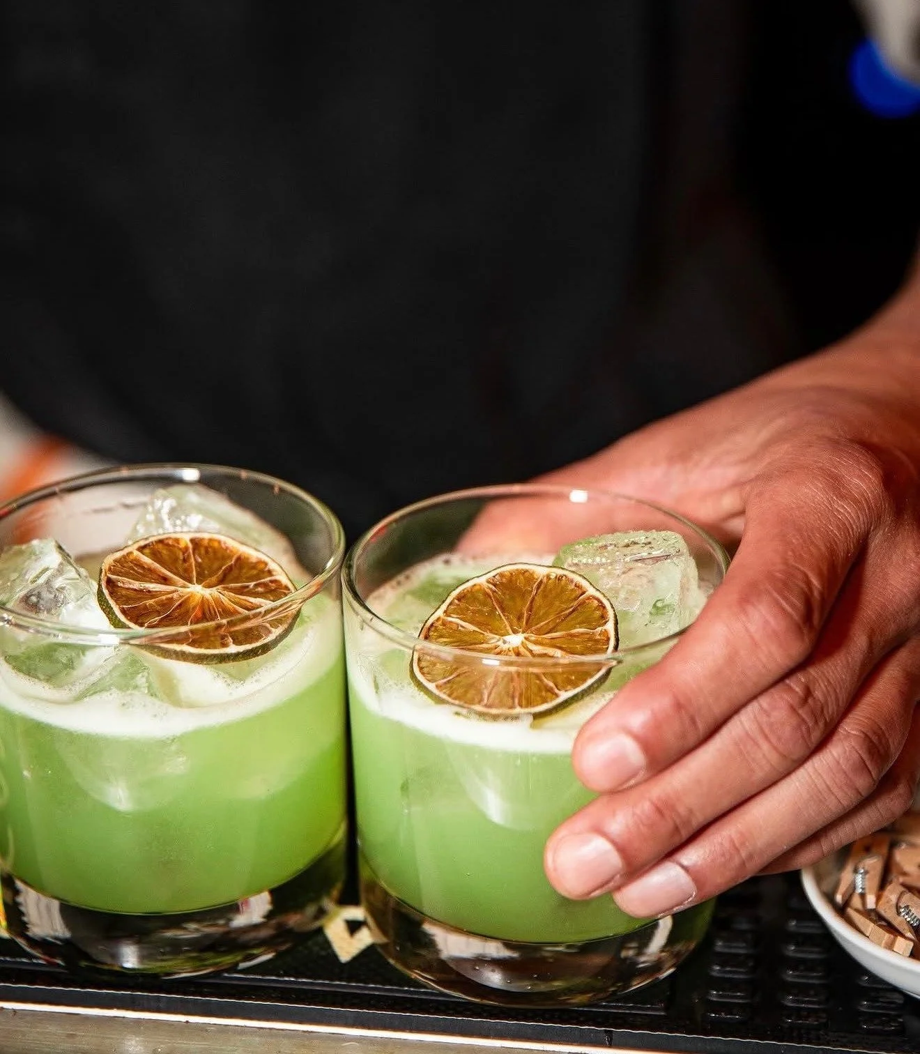 Two green iced drinks garnished with dried citrus slices, one held by a hand.