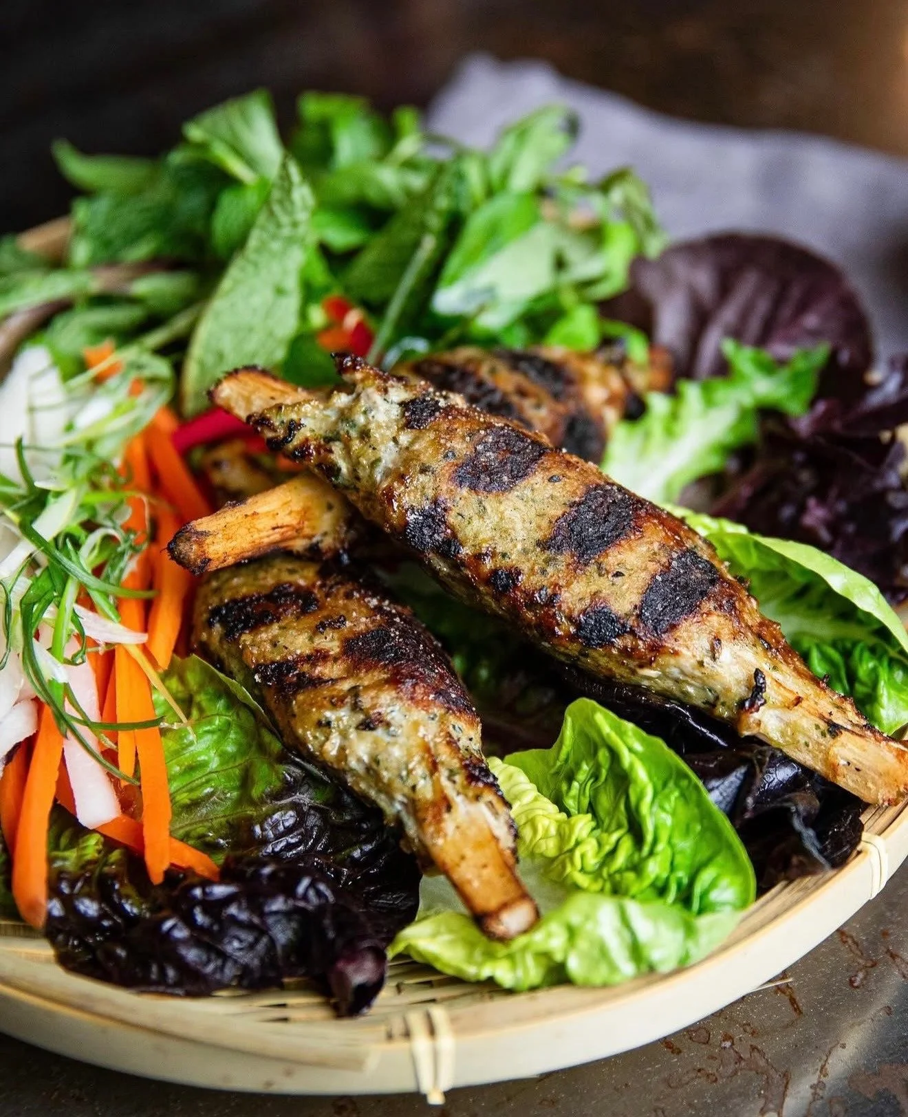 Grilled skewers served with lettuce, fresh herbs, and thinly sliced vegetables.