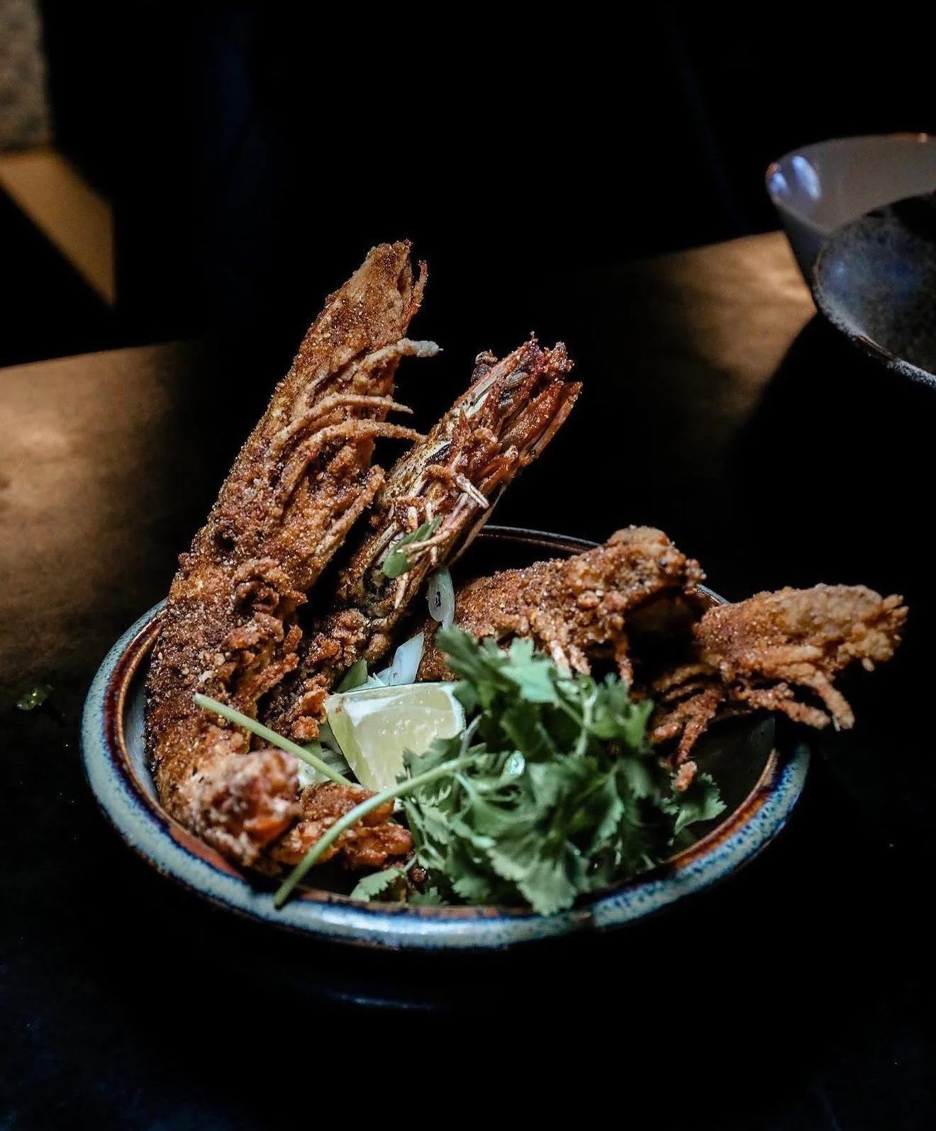 Fried whole shrimp with cilantro and a lime wedge in a blue-rimmed bowl.
