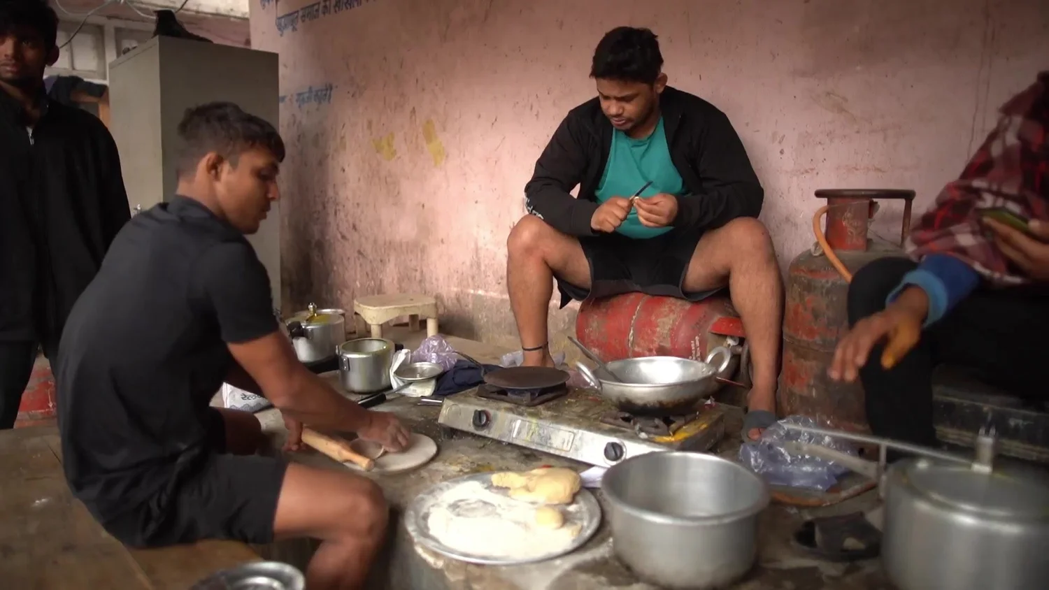 Wrestlers cook rotis on a gas stove between sessions