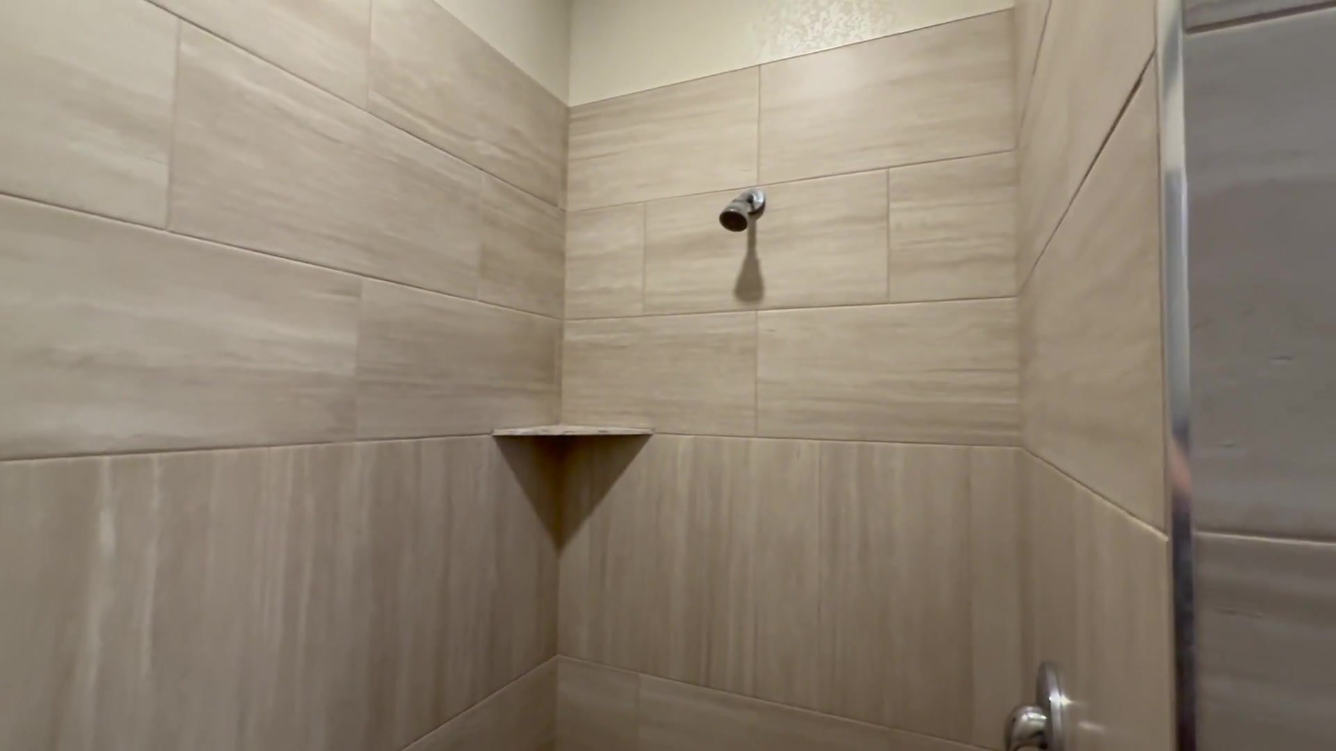 Tiled shower with a chrome showerhead and corner shelf at Woods and River RV Park