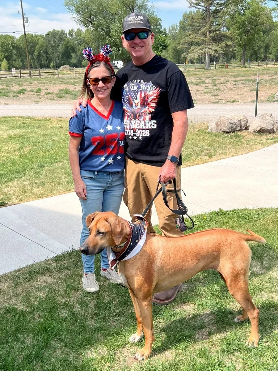 Two guests standing with their dog on the campground lawn.