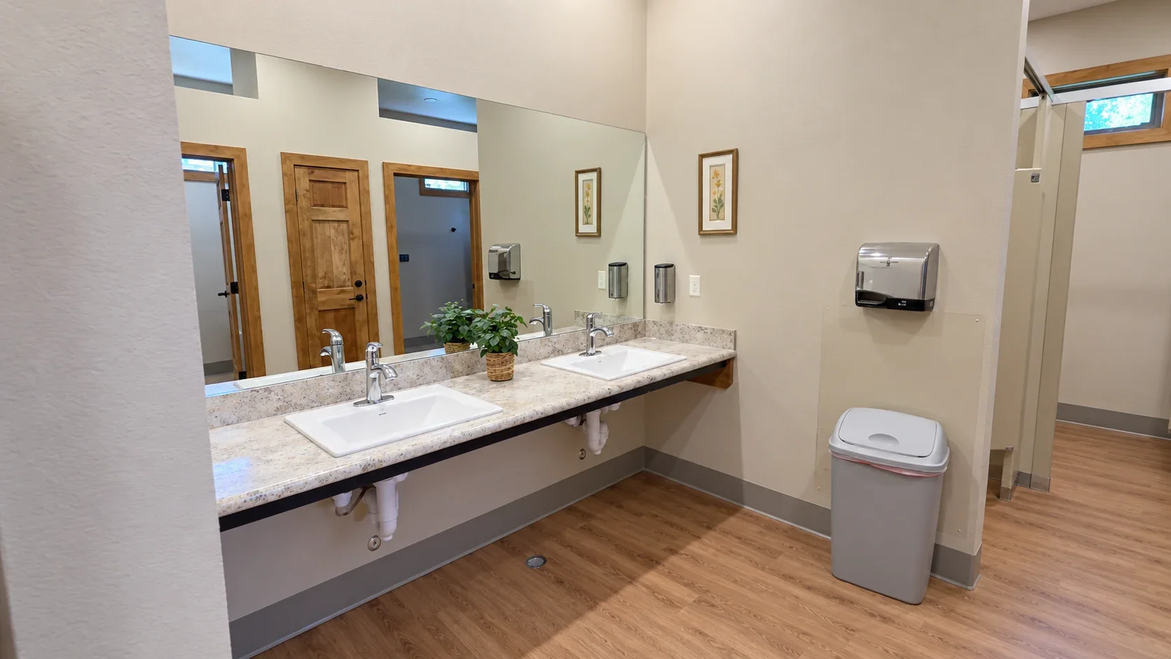 Bathroom vanity with two sinks, a large mirror and wood-look flooring at Woods and River RV Park