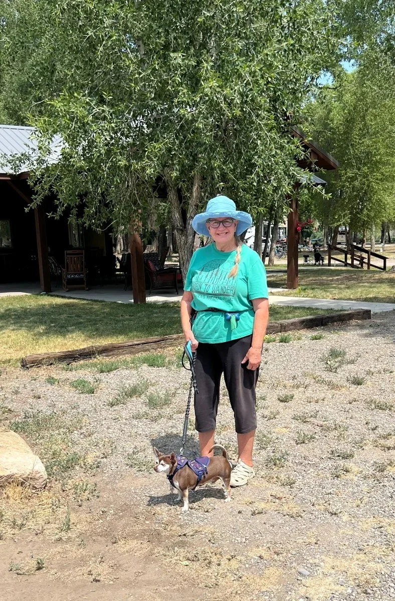 A guest standing with a small dog beneath the campground trees.