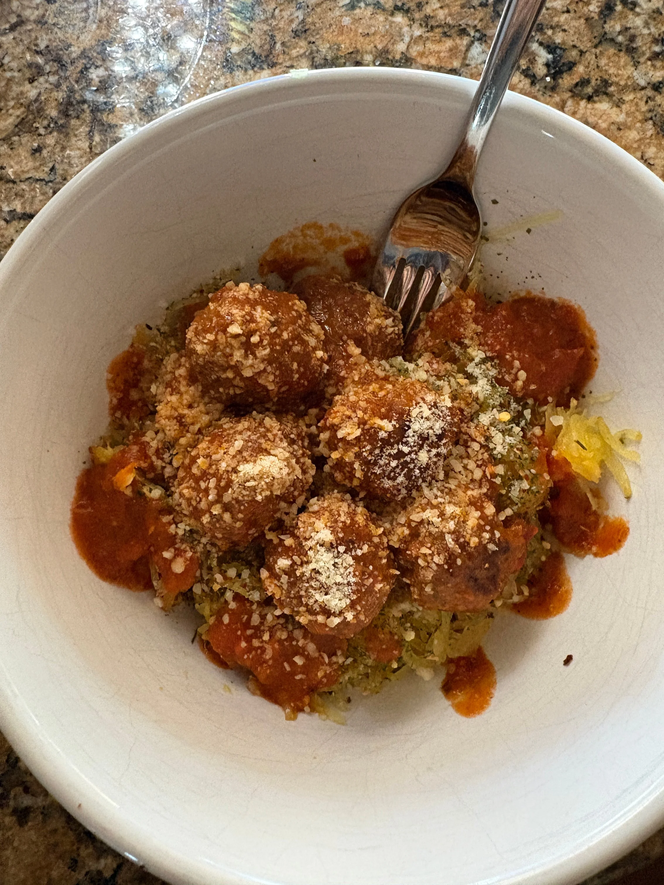 Saucy meatballs in a white bowl topped with grated cheese and herbs.