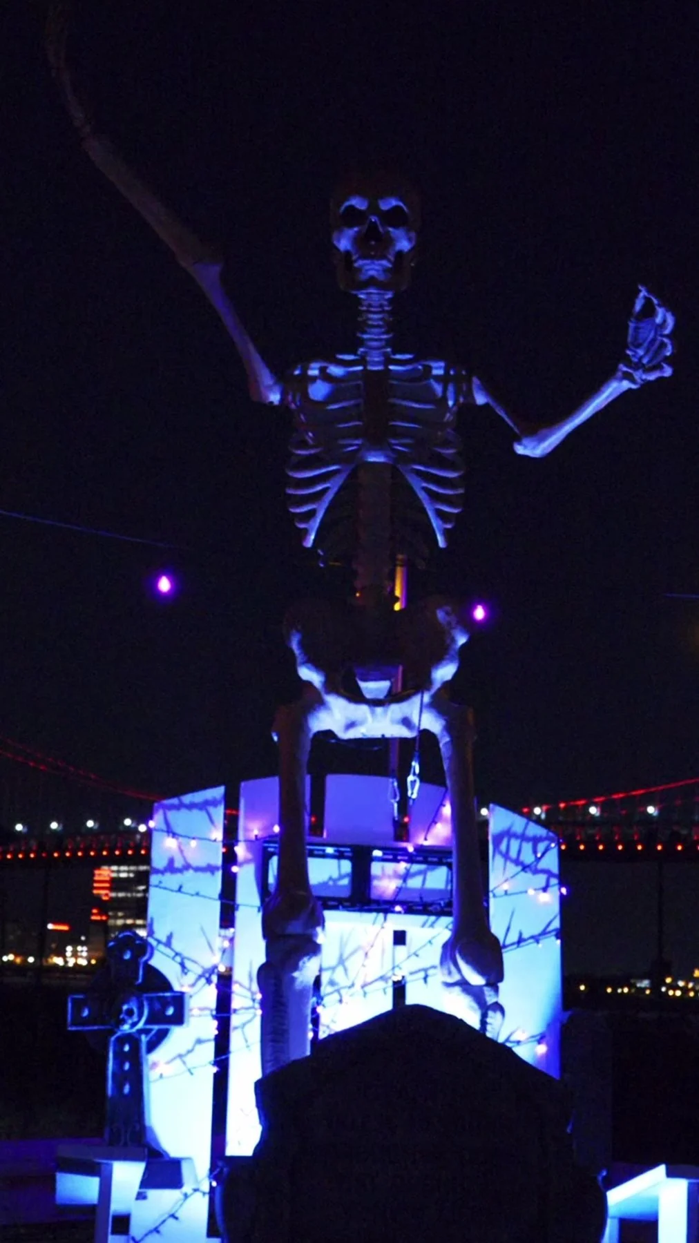 Giant illuminated skeleton on the River Deck with the Benjamin Franklin Bridge behind it