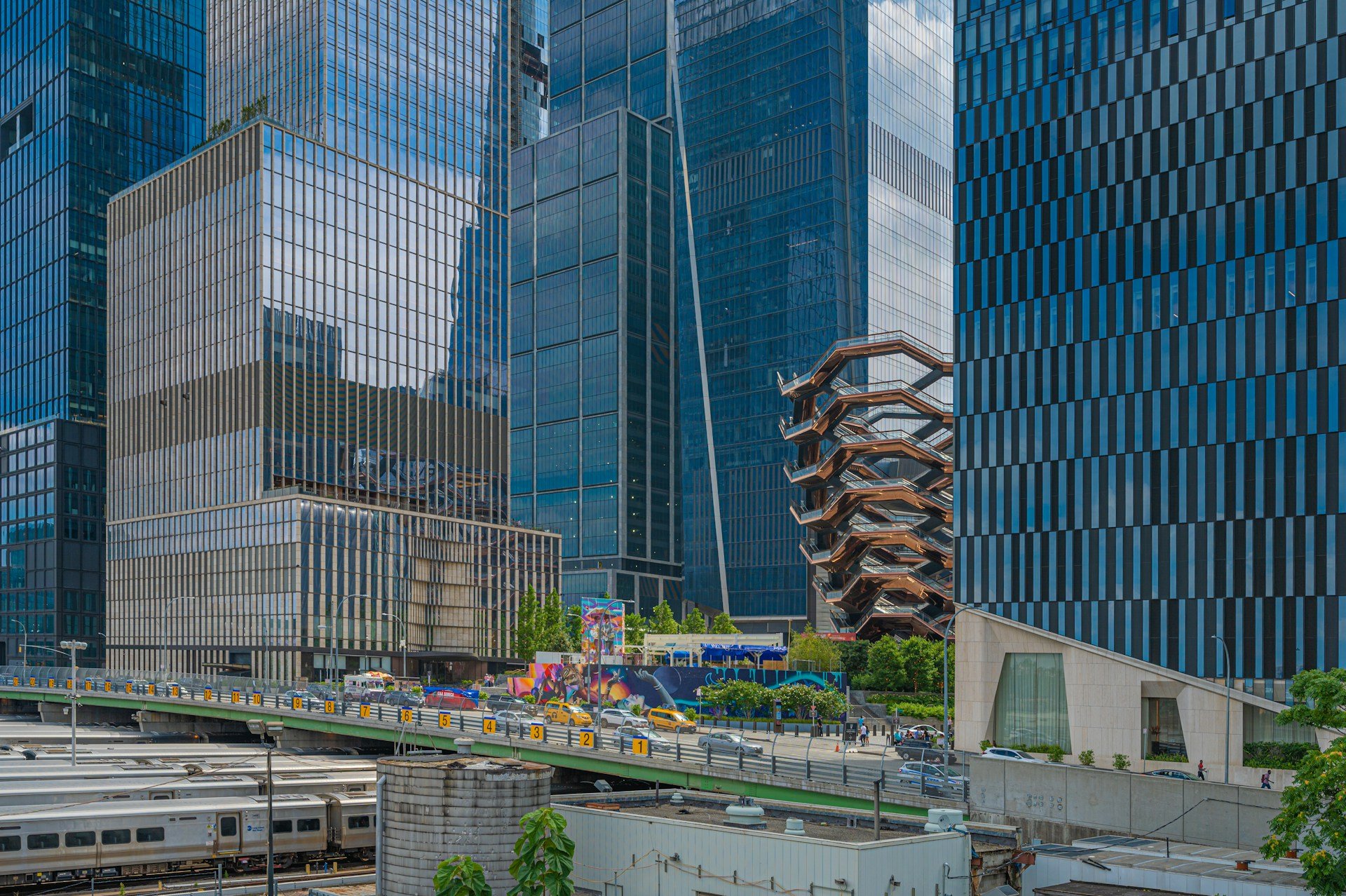A train moves through an urban landscape dominated by buildings, highlighting the Hudson Yards real estate area.