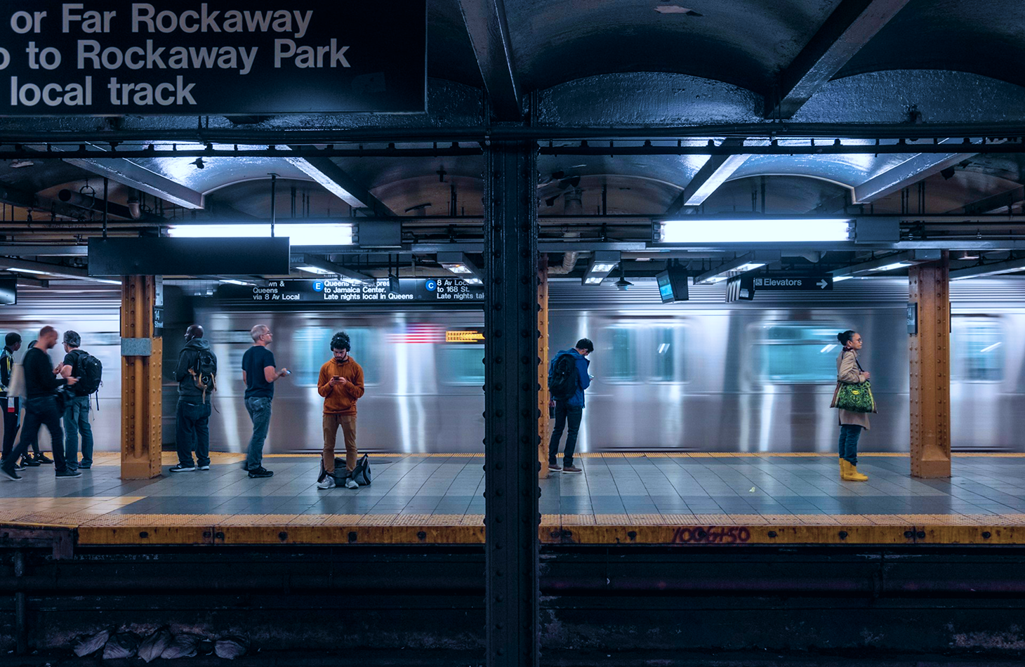 People waiting at a subway station, observing public safety measures while anticipating their train's arrival.