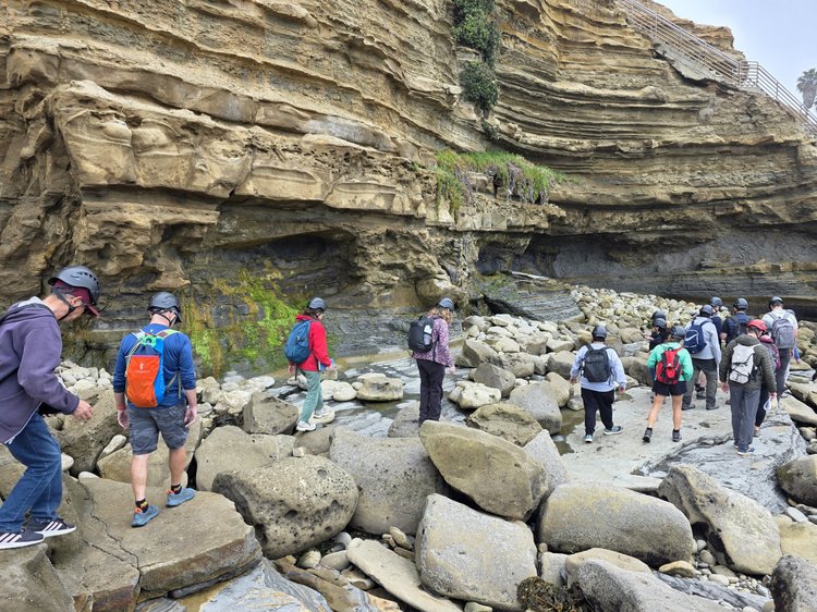 Students scrambling under towering layered cliff
