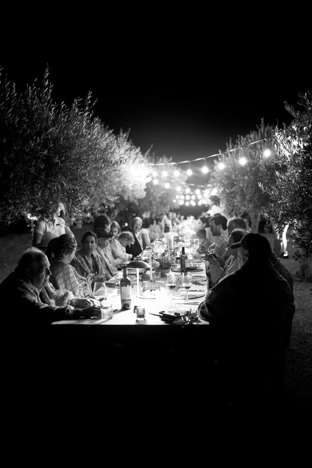 Black and white view of guests at dinner beneath strings of lights.