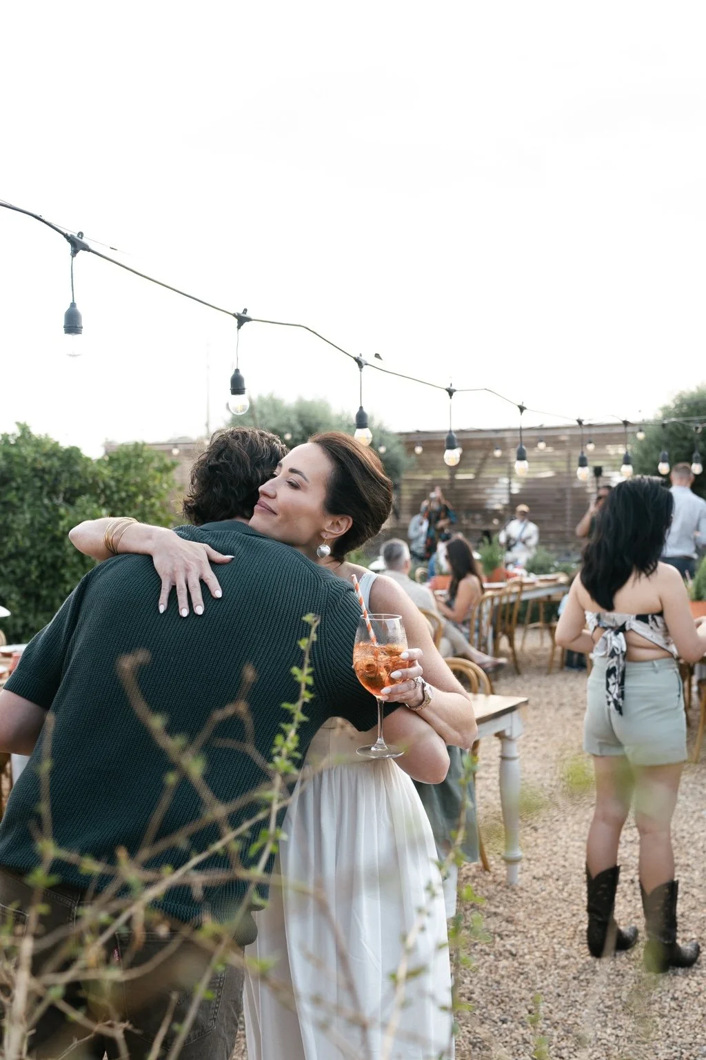 Joanna greeting a guest beneath strings of outdoor lights.