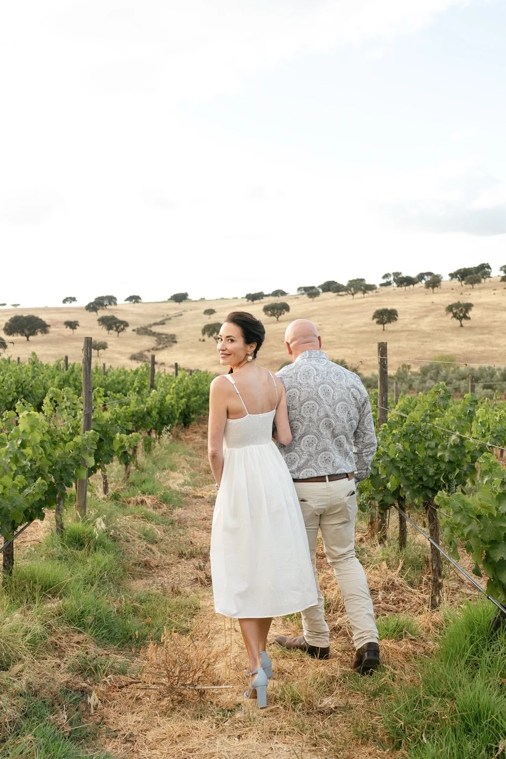 Joanna and Greg walking between rows of vines on the day before the wedding.