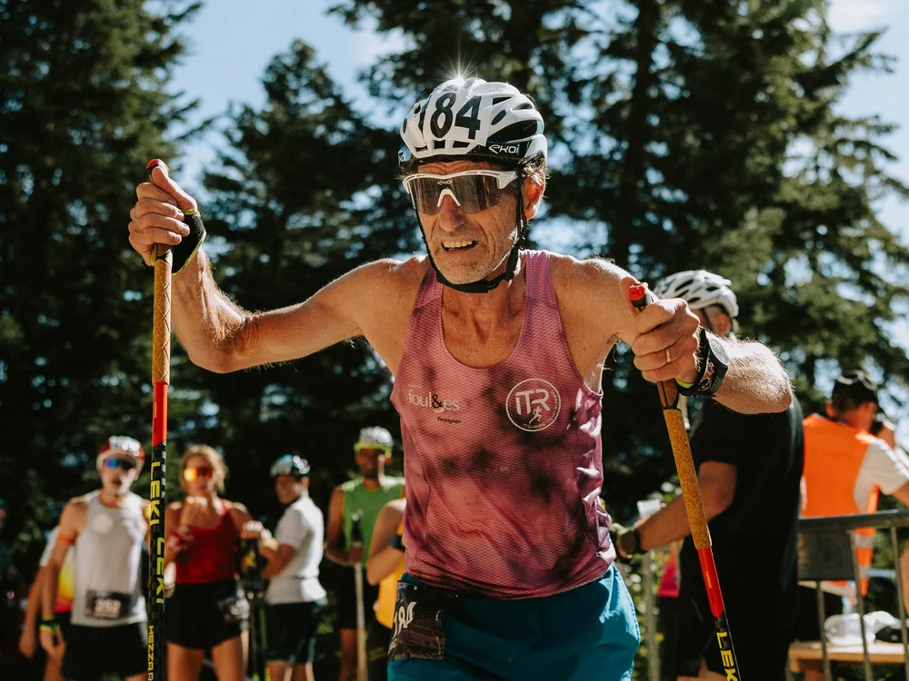 Un coureur avec dossard et bâtons, souriant, dans la montée du KV.